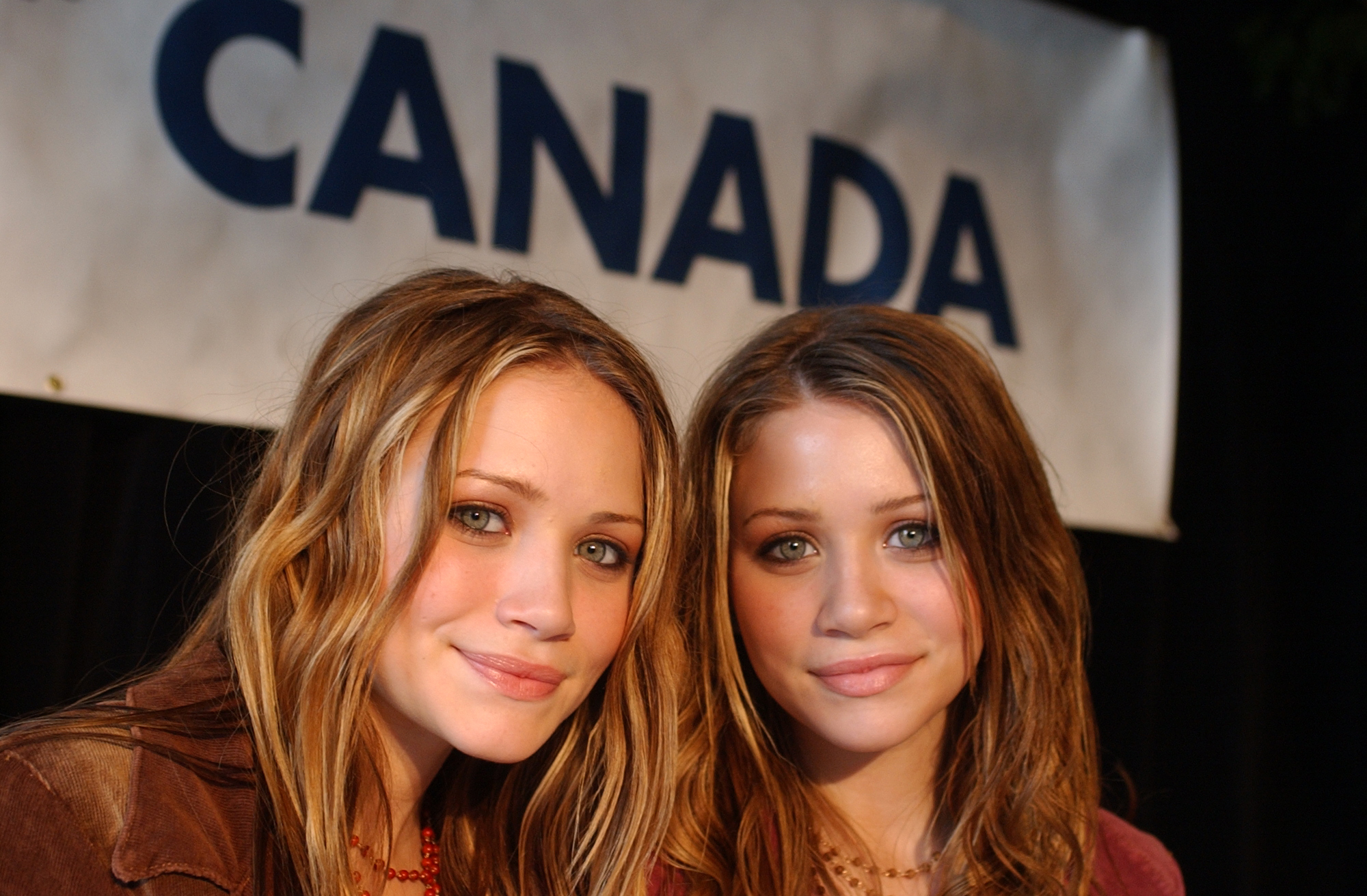 Professional poise and confident, warm smiles defined the twins at 15 years old on April 2, 2002, displaying softer, face-framing honey-blonde layers and earthy makeup tones at a Canadian press conference while promoting their Wal-Mart clothing venture.
