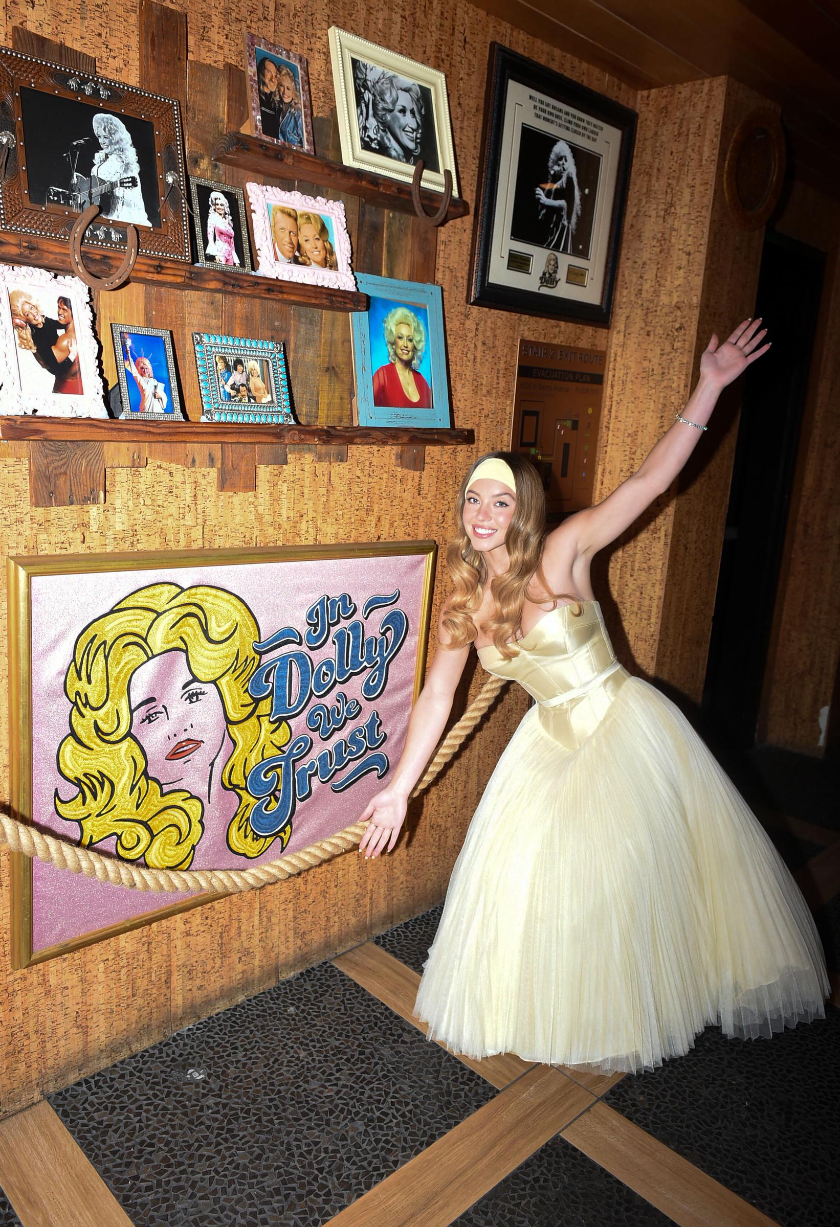 Sydney Sweeney strikes a playful freestyle pose, adding movement to the frame. Her ivory gown sways slightly, revealing the layers of tulle beneath the structured bodice. The headband stays in place, anchoring the look with a touch of charm.
