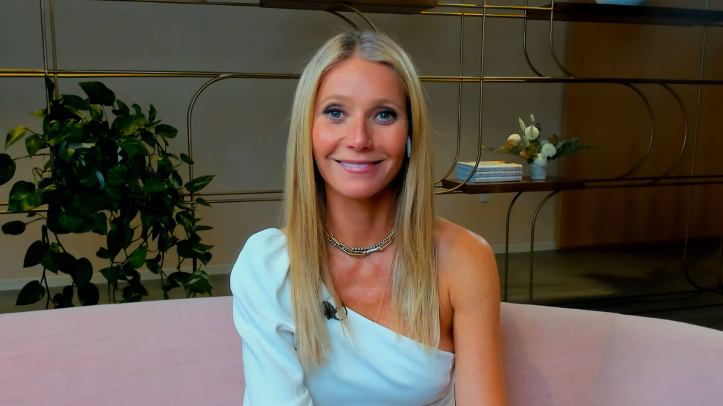 Gwyneth Paltrow appears on "Watch What Happens Live With Andy Cohen" in 2021. She wears a chic one-shoulder white top paired with a gold chain necklace. Her straight blonde hair is parted in the middle and worn sleek, while soft makeup and a rosy lip keep her look modern and effortlessly polished for the television appearance.