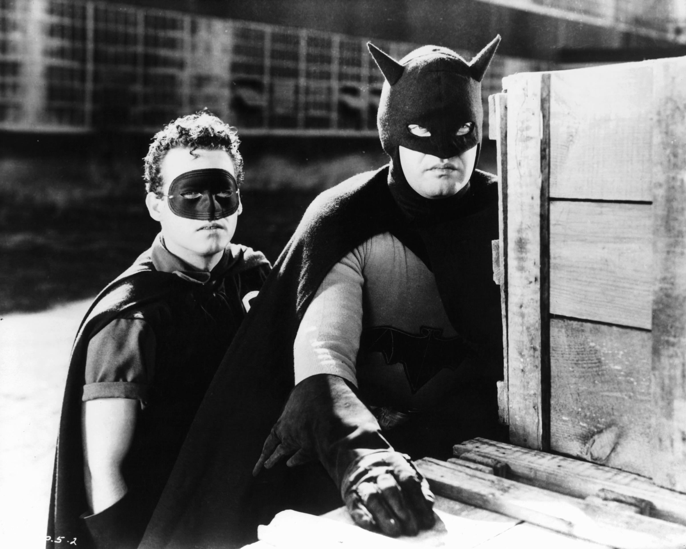 Douglas Croft as Robin and the first live-action Batman hide behind crates during a scene from Columbia Pictures' 1943 "Batman" serial. | Source: Getty Images