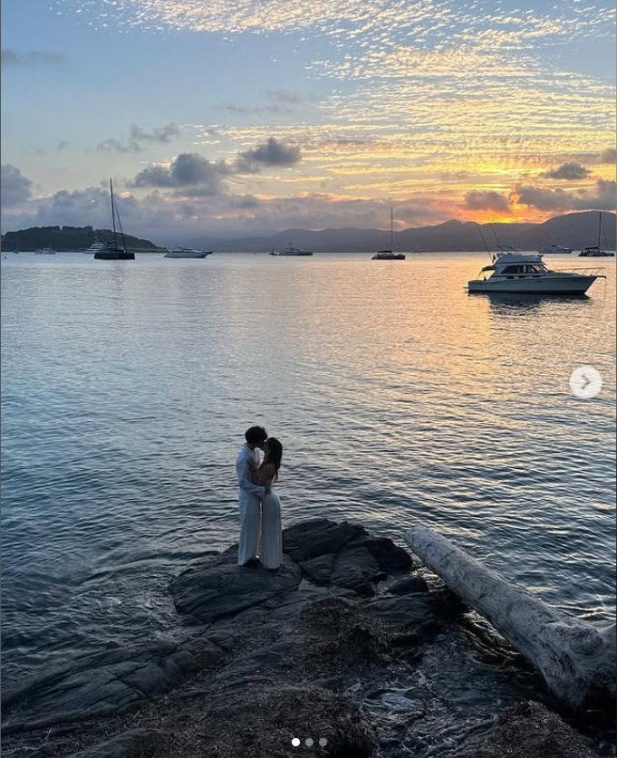 Dylan Lee and Paula Bruss shared a kiss on the rocky shoreline in a romantic 2024 photo, with the sunset and boats scattered across the water behind them. | Source: Instagram/babybruss