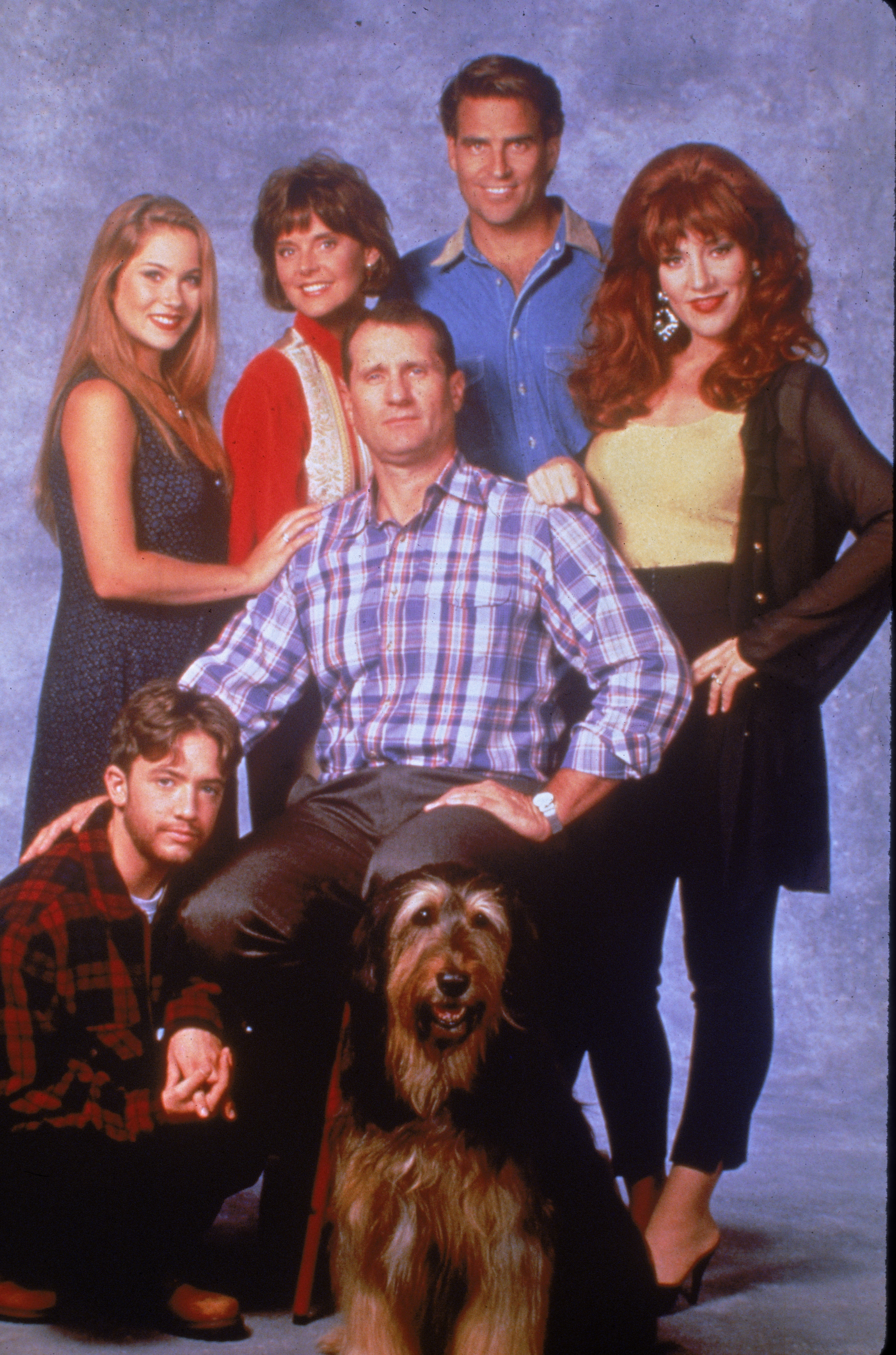 The ensemble cast of "Married... with Children"—including David Faustino, Christina Applegate, Amanda Bearse, Ed O'Neill, Ted McGinley, and Katey Sagal—posed together with their beloved family dog, Buck, for a promotional studio portrait circa 1994. Anchored by O'Neill seated front and center in a plaid button-down and Faustino kneeling beside him, the group captured the signature dysfunctional dynamic of television's favorite suburban family alongside their eccentric neighbors. | Source: Getty Images