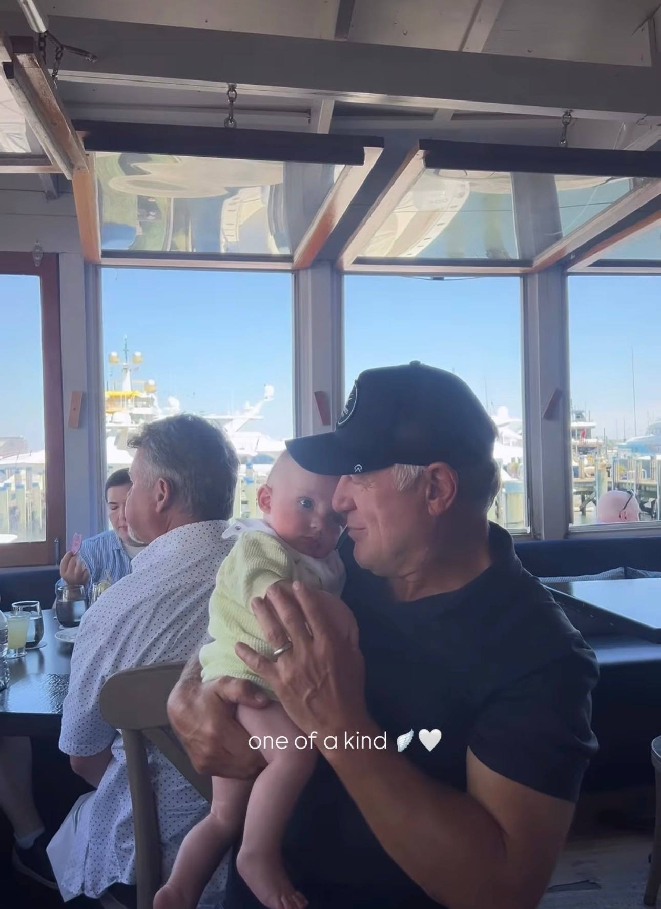 Claude Lemieux cradles a baby while dining at a waterfront restaurant in a photo shared by Kate Monahan. | Source: Instagram Story/klmonahan