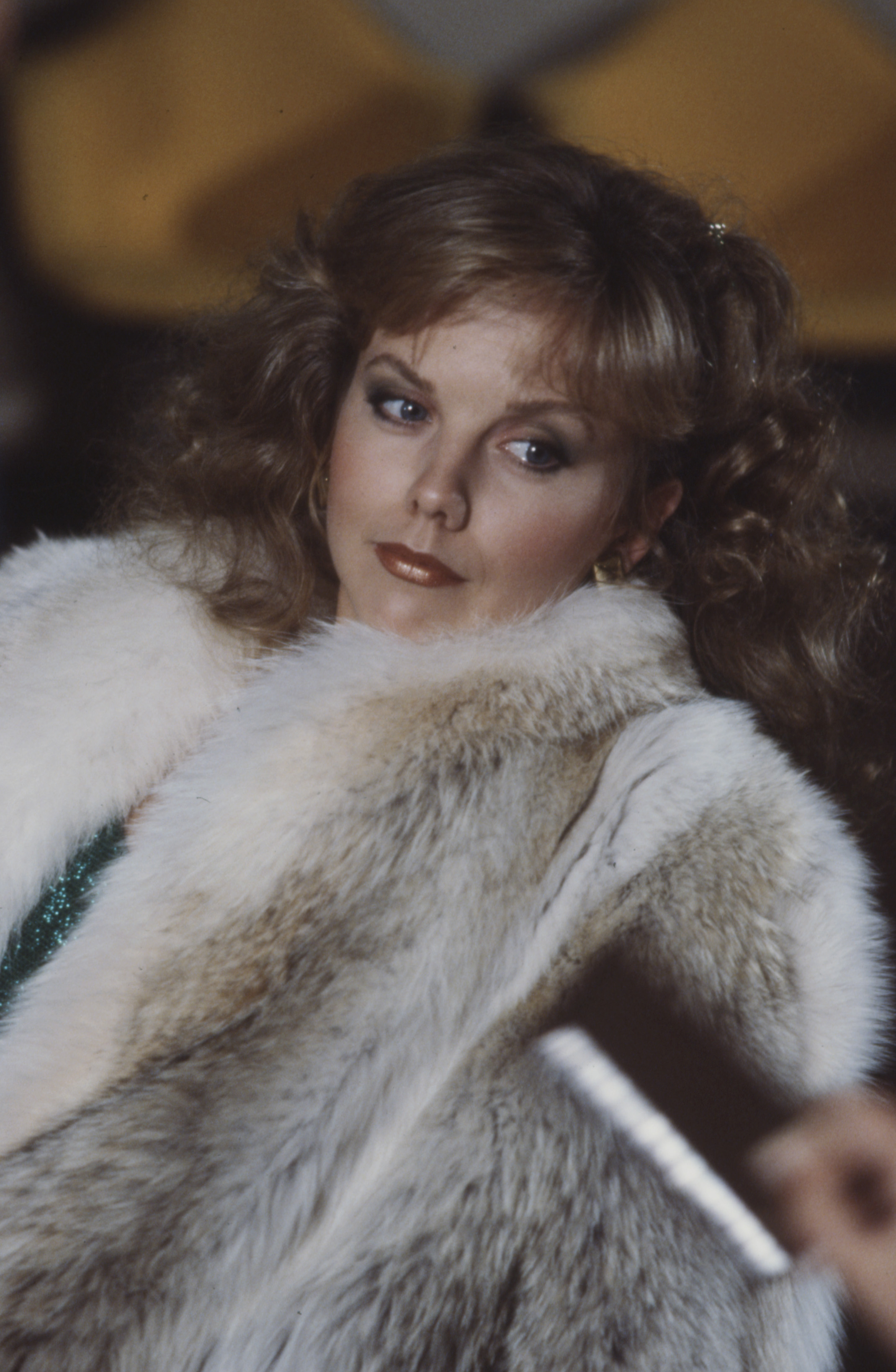 Draped in an opulent, fluffy fur coat over a hint of sparkling emerald green, a 26-year-old Linda Purl fully embraced 1980s television melodrama for "Money on the Side" in Los Angeles. Her face took on a mature, sultry contour accented by defined smoky eyeshadow, glossy rust lips, and voluminous, feathered brunette curls cascading down her shoulders.