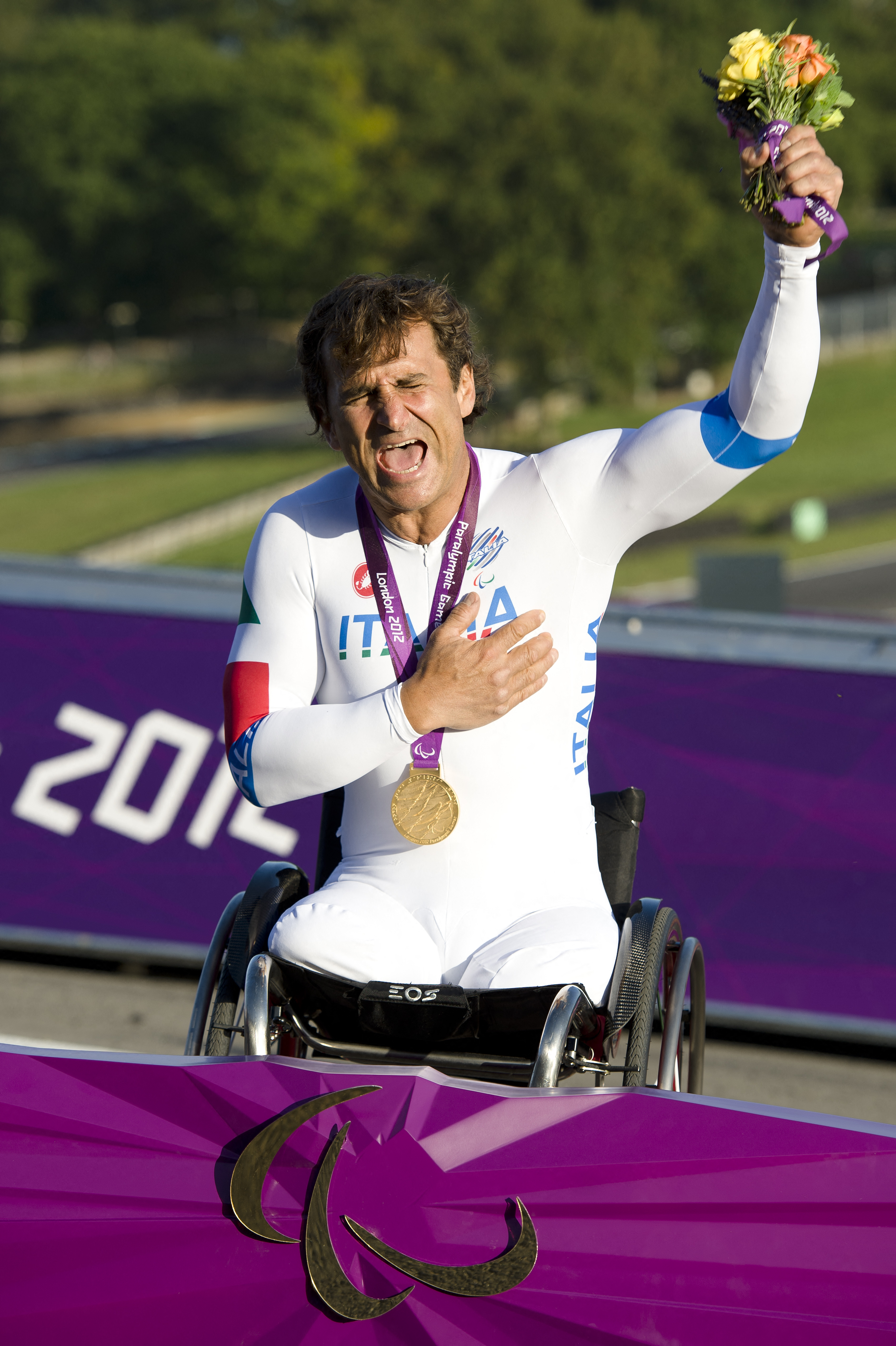 Alex Zanardi, wearing his gold medal, sings the Italian national anthem on the podium after winning the men's individual H4 time trial cycling final during the London 2012 Paralympic Games at Brands Hatch circuit in Kent, southern England, on September 5, 2012. | Source: Getty Images