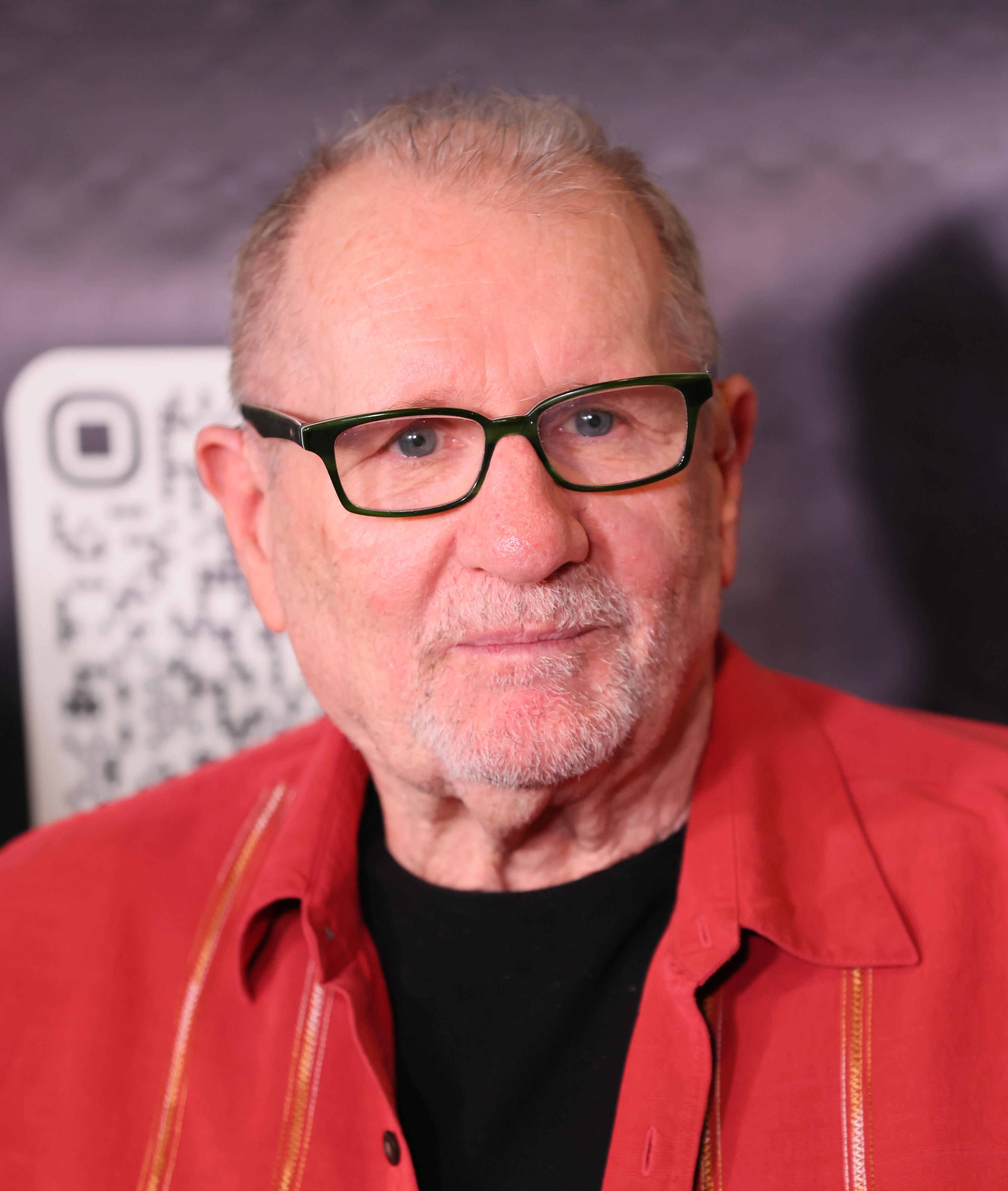 Ed O'Neill posed for a warm close-up portrait while attending the opening night of "Proof" at the El Portal Theater on July 24, 2026, in North Hollywood, California. Sporting forest-green rectangular glasses and a neatly trimmed silver beard, the veteran actor added a splash of color to the red carpet in a vibrant coral-red collared shirt layered over a simple black tee as he arrived to support the stage production. | Source: Getty Images