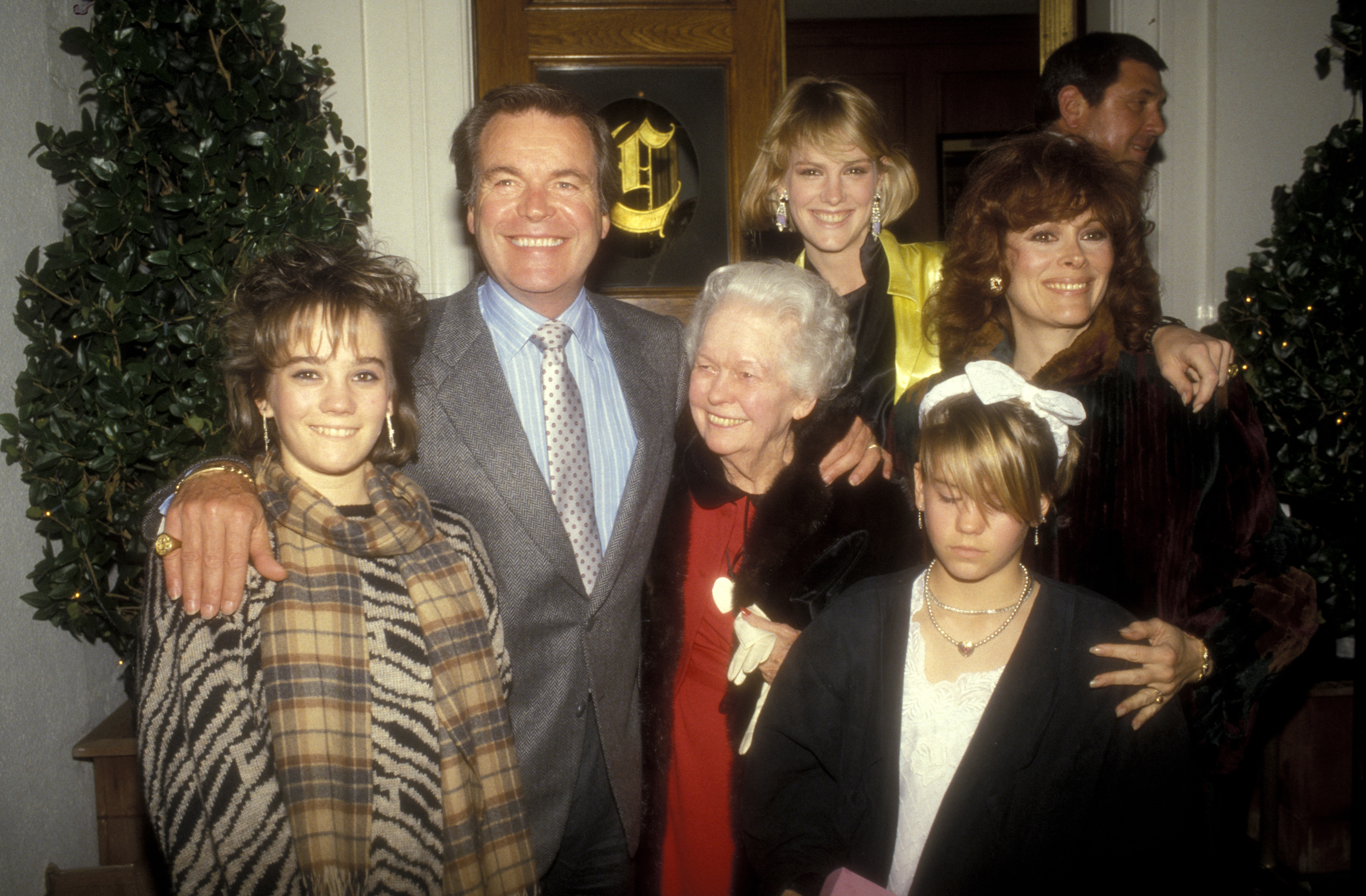 Robert Wagner poses with wife Jill St. John, his mother, and daughters Katie, Natasha, and Courtney Wagner at a Valentine’s Day party in 1985. Robert stands smiling in a suit and tie, while the family gathers closely around him, dressed in festive attire for the occasion.