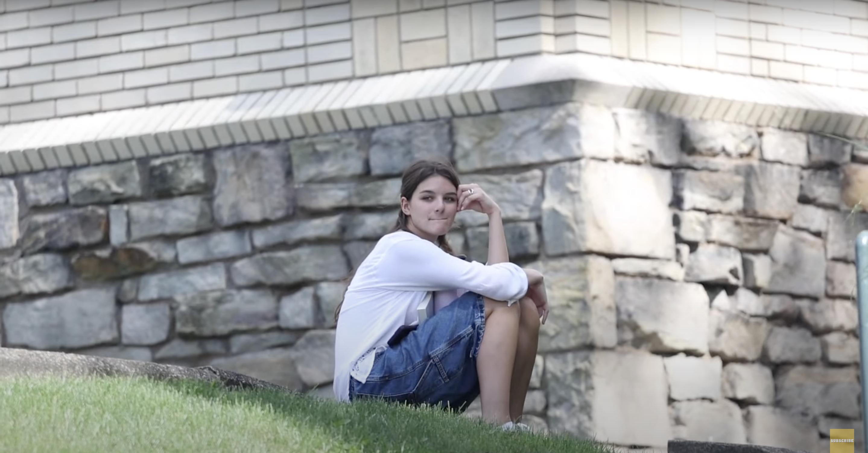 Suri Cruise is captured seated quietly on a patch of grass, surrounded by the calm of a campus setting. Her gaze drifts off into the distance, lost in thought. Source: YouTube/pagesix