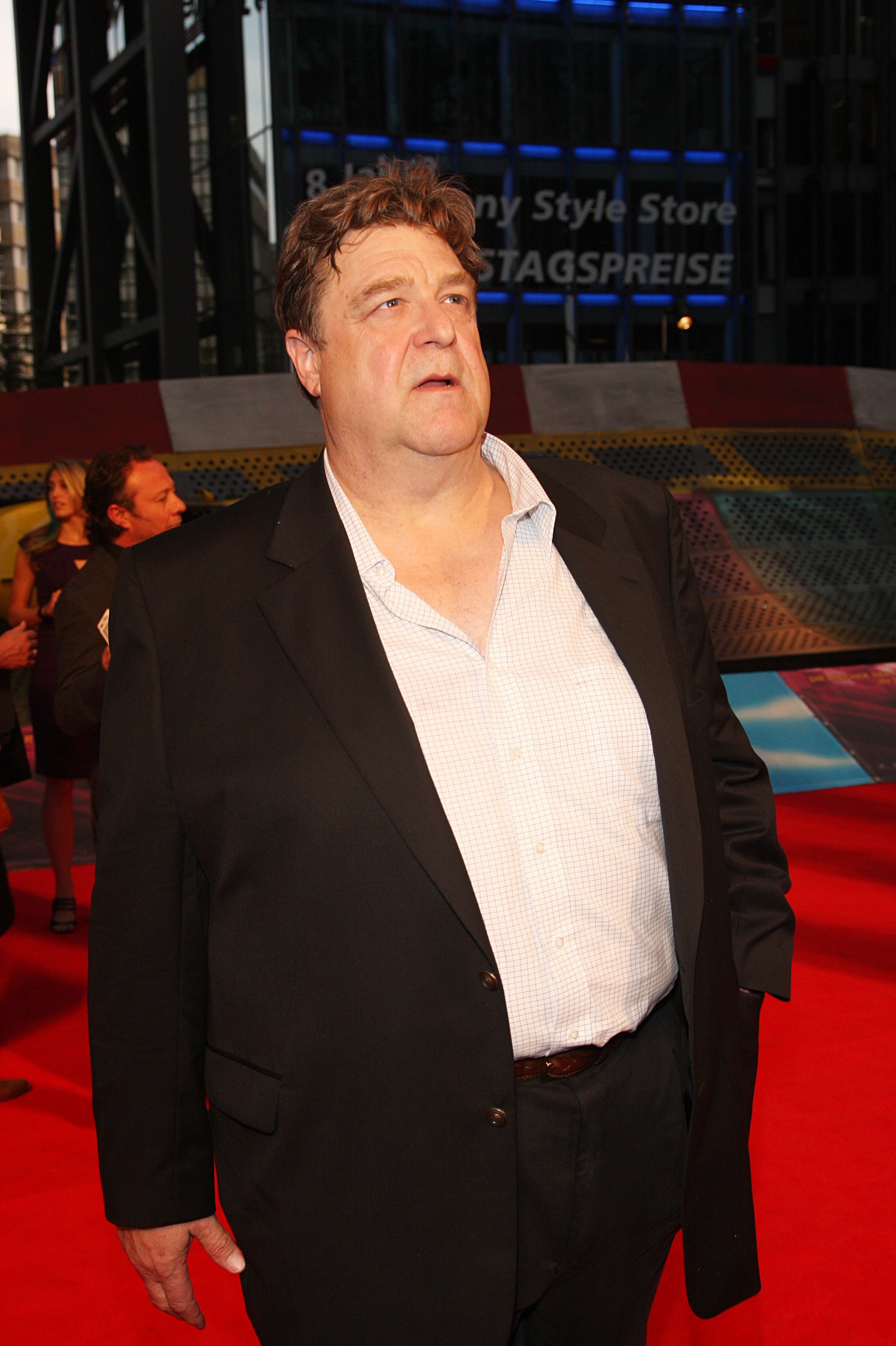 At the "Speed Racer" European premiere at CineStar at Potsdamer Platz in Berlin, Goodman stepped on the red carpet in a white shirt, unbuttoned at the top, tucked into a black suit. He was caught on camera looking up at something.