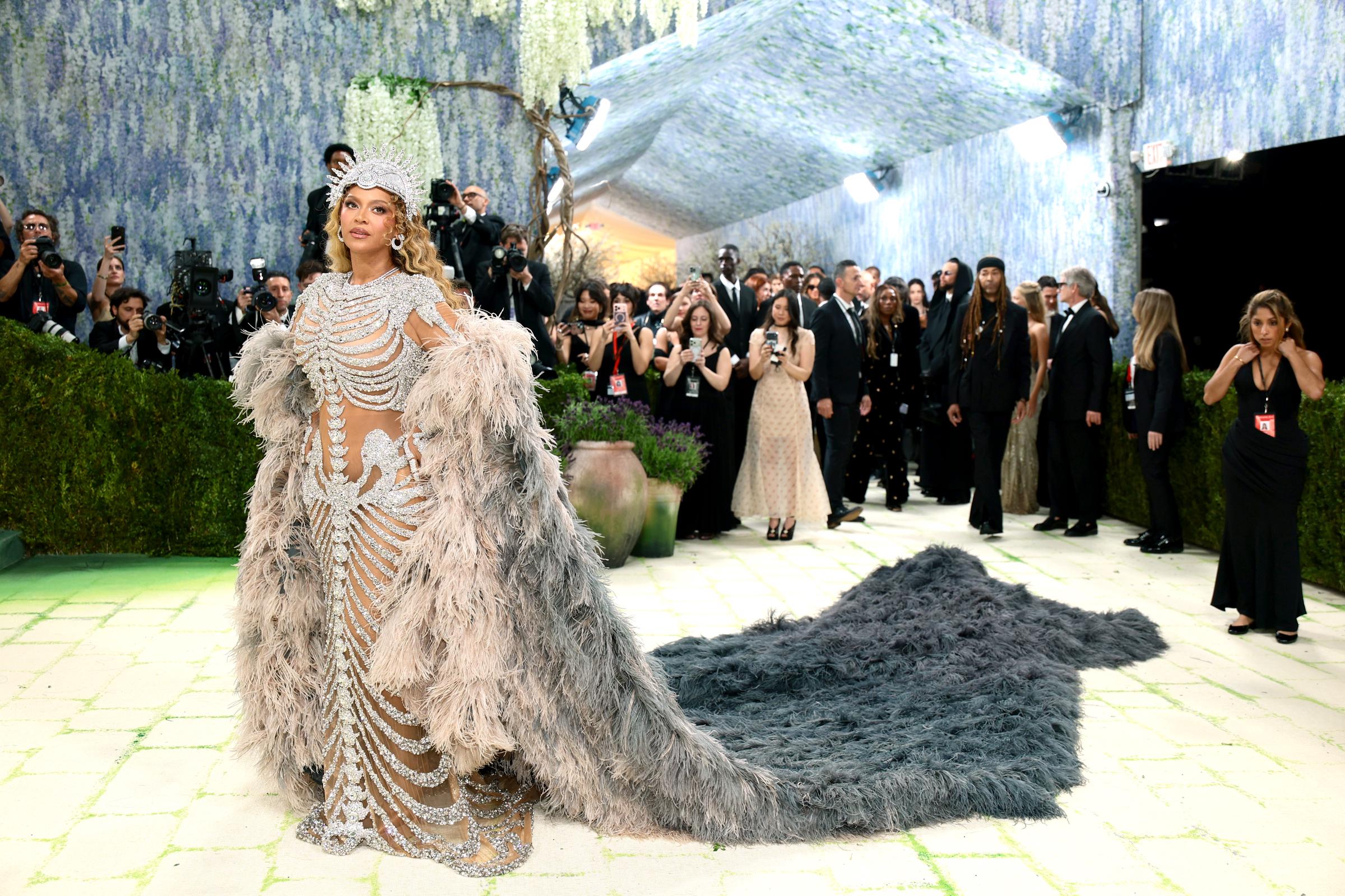 Beyoncé’s gray feathered train stretches across the carpet behind her | Source: Getty Images