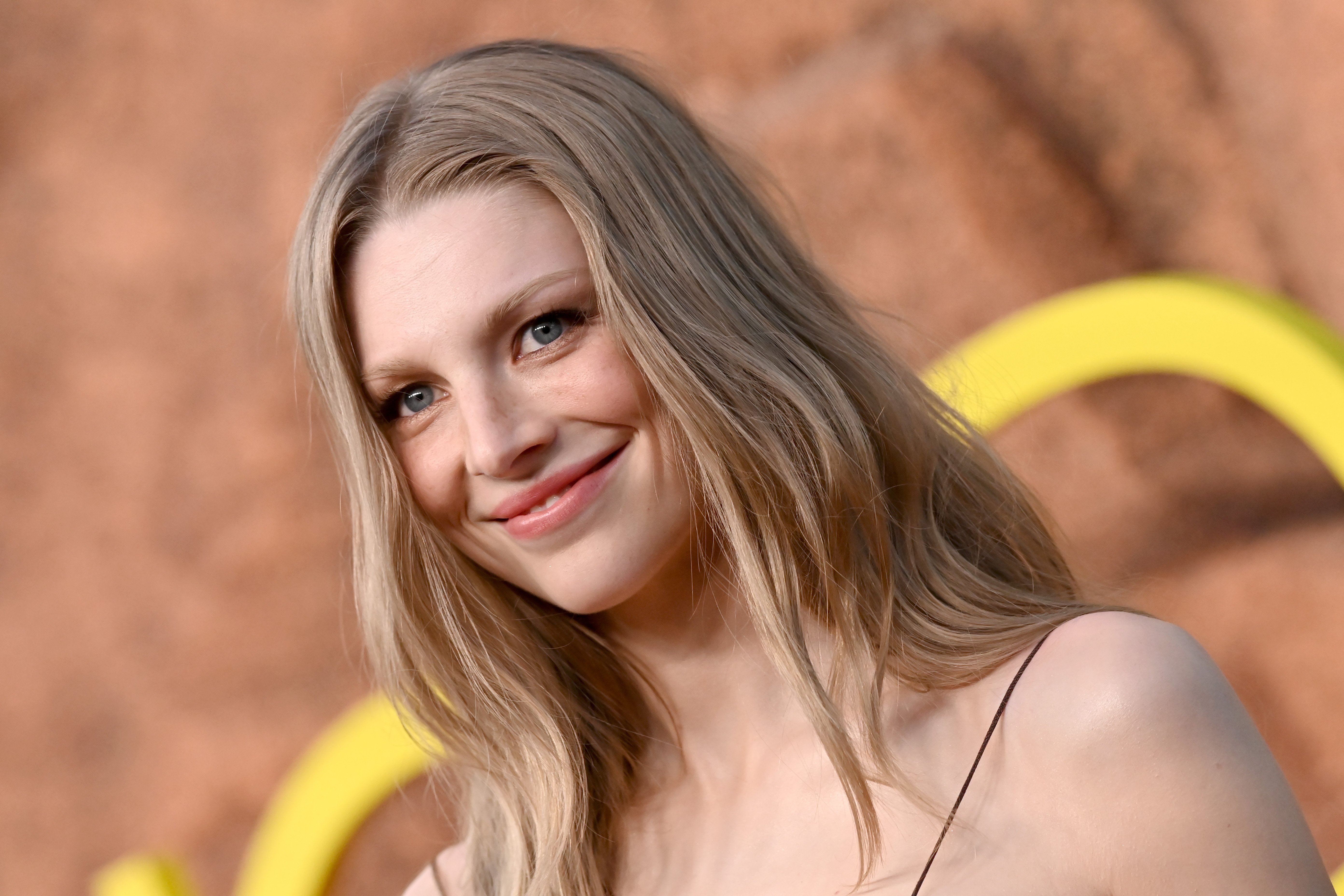 Hunter Schafer softens the red carpet moment with an understated, luminous presence, her delicate features framed by long, flowing blonde hair and minimal makeup that lets her natural glow take center stage, creating a look that feels effortlessly serene and quietly captivating.