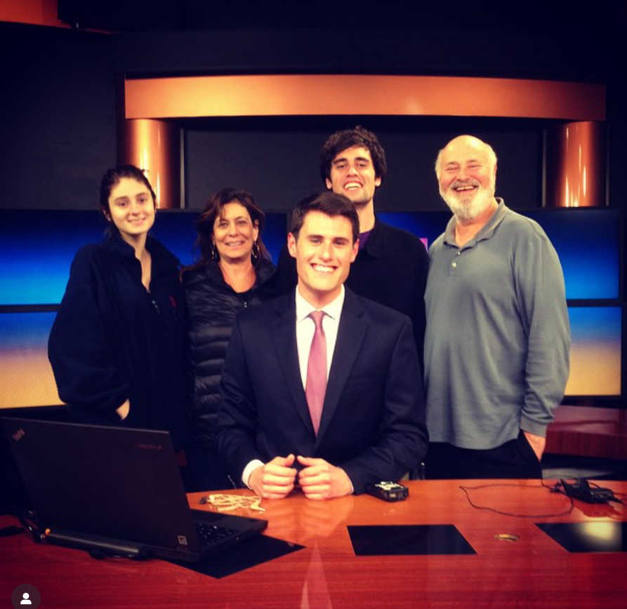 Jake Reiner's family, Rob, Michele, Romy, and Nick, pose with him inside a television news studio as he sits smiling at the anchor desk, from a post dated January 20, 2015. | Source: Instagram/jakereiner