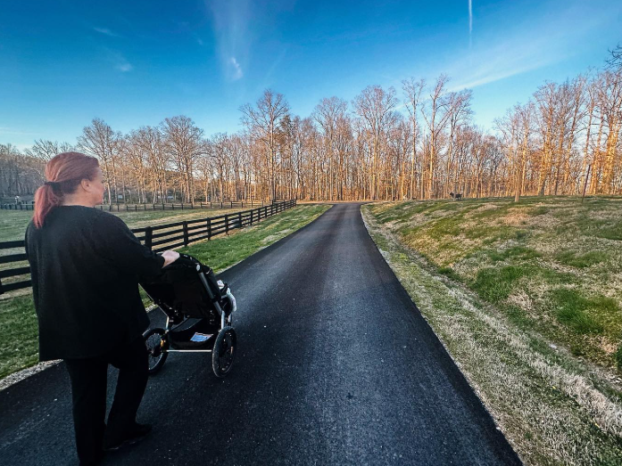 Wynonna pushes a stroller along a paved driveway bordered by a wooden fence, grassy fields, and tall trees. The peaceful country setting offers a glimpse of the everyday surroundings where she is raising her granddaughter, Kaliyah. | Source: Instagram/wynonnajudd