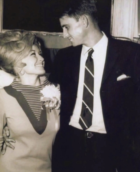 Parton looked up at Dean with a smile as he wrapped an arm around her in this black-and-white photograph from their younger years. Their affectionate pose captured a side of the singer's personal life that remained largely removed from her highly visible career. While Parton became recognizable around the world, Dean consistently avoided the spotlight and rarely appeared publicly alongside his famous wife. | Source: Facebook/One Country