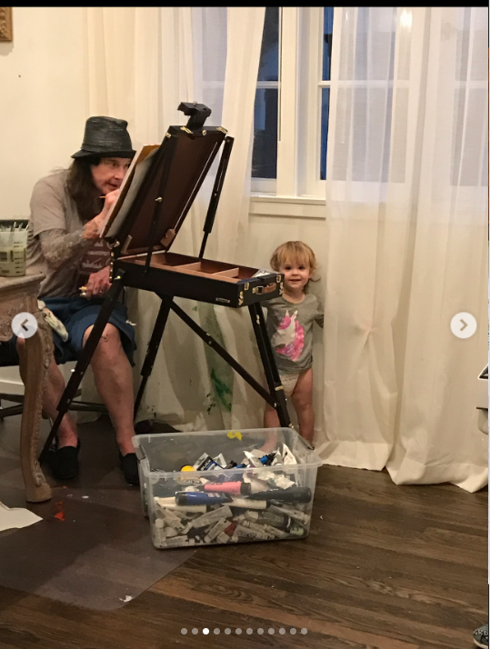 Ozzy Osbourne paints as his grandchild peaks from behind a curtain, from a post dated July 24, 2025 | Source: Instagram/lisastelly