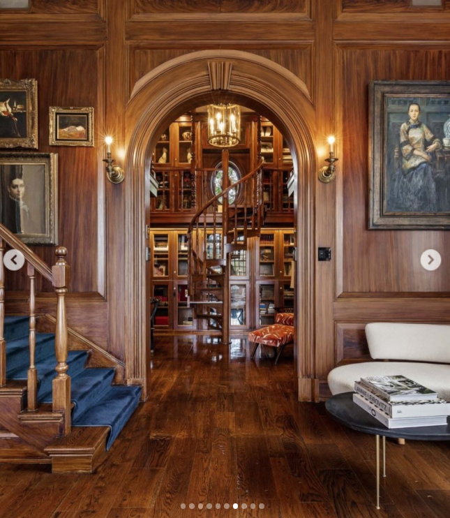 An arched doorway offers a direct view into the wood-paneled library, where floor-to-ceiling shelving surrounds a spiral staircase. The intricate woodwork and framed portraits help explain why the home's traditional interiors became such a talking point among viewers. | Source: Instagram/rogerperrygroup