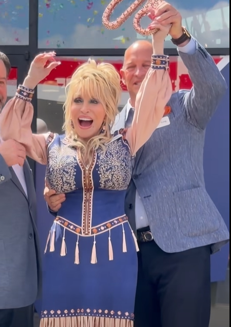 Dolly Parton stands between two men during the ribbon-cutting ceremony, a moment that prompted social media users to speculate about whether they were helping support her.