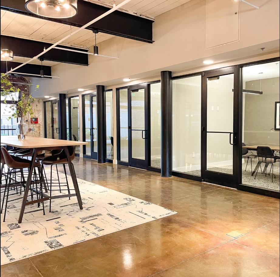 The communal area continues along a row of glass-fronted rooms and workspaces, with high-top seating and a long table adding to the loft's open, contemporary feel. | Source: Facebook/Judson Mills Loft