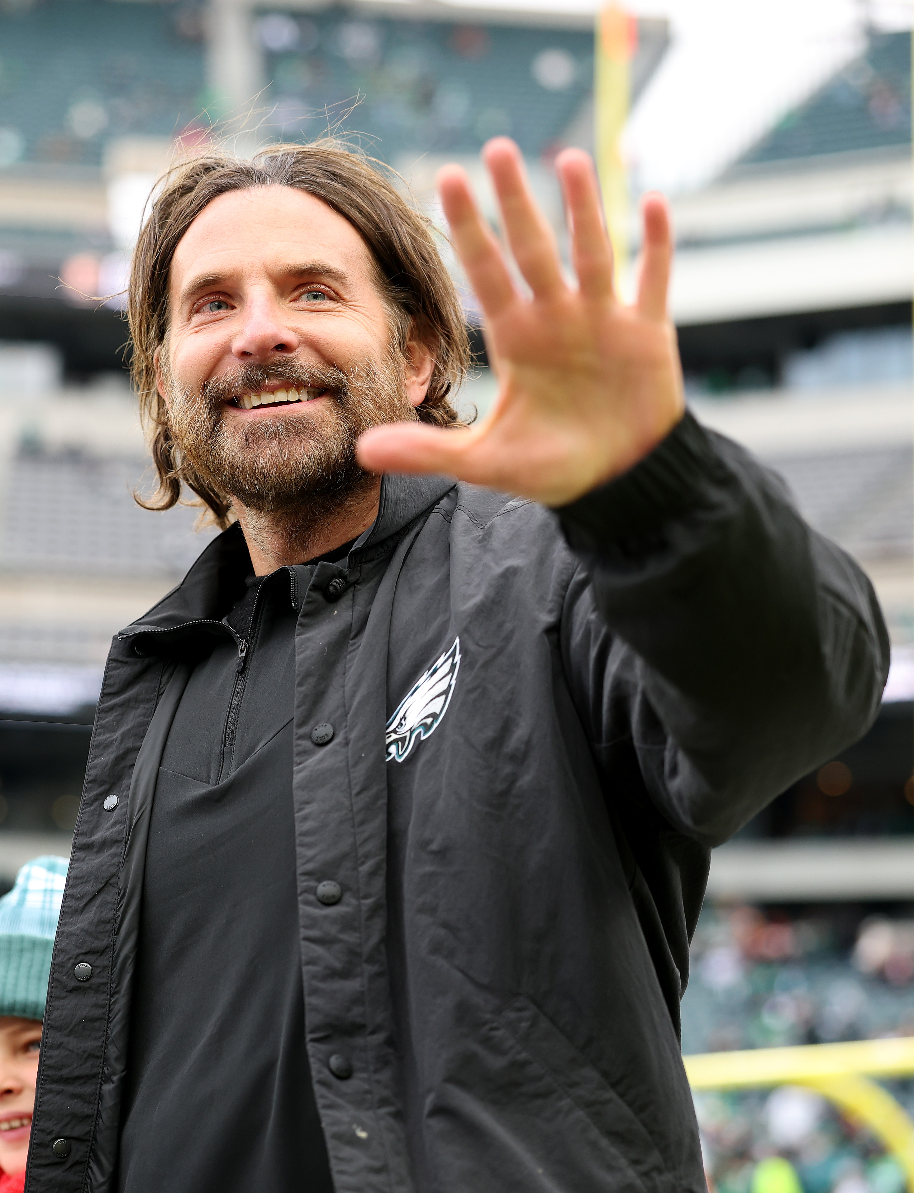 Cooper conveyed a warm expression with his eyes crinkling at the corners as he raised his hand in a wave, showcasing a full beard with prominent streaks of gray. However, his facial skin looks noticeably smoother than in earlier photos. This was taken during the NFC Championship Game between the Washington Commanders and the Philadelphia Eagles at Lincoln Financial Field on January 26, 2025, in Philadelphia, Pennsylvania.