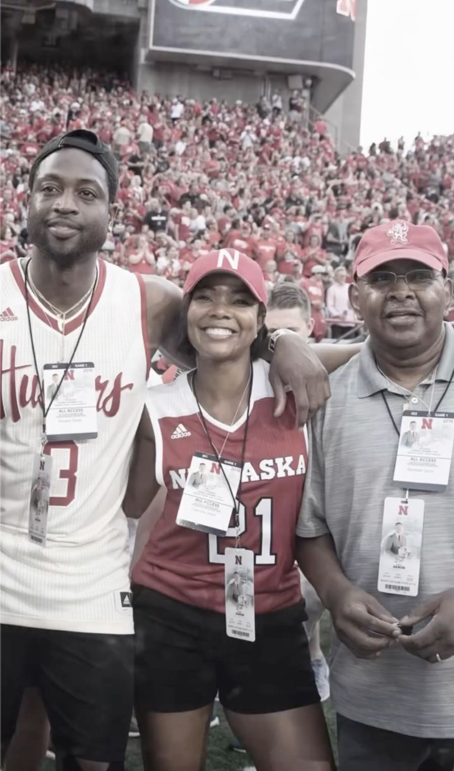 In a stadium setting filled with fans dressed in red, Gabrielle stands between Dwyane Wade and her father, Sylvester Union. All three wear event credentials, suggesting a special access or game-day experience. | Source: Instagram/gabunion