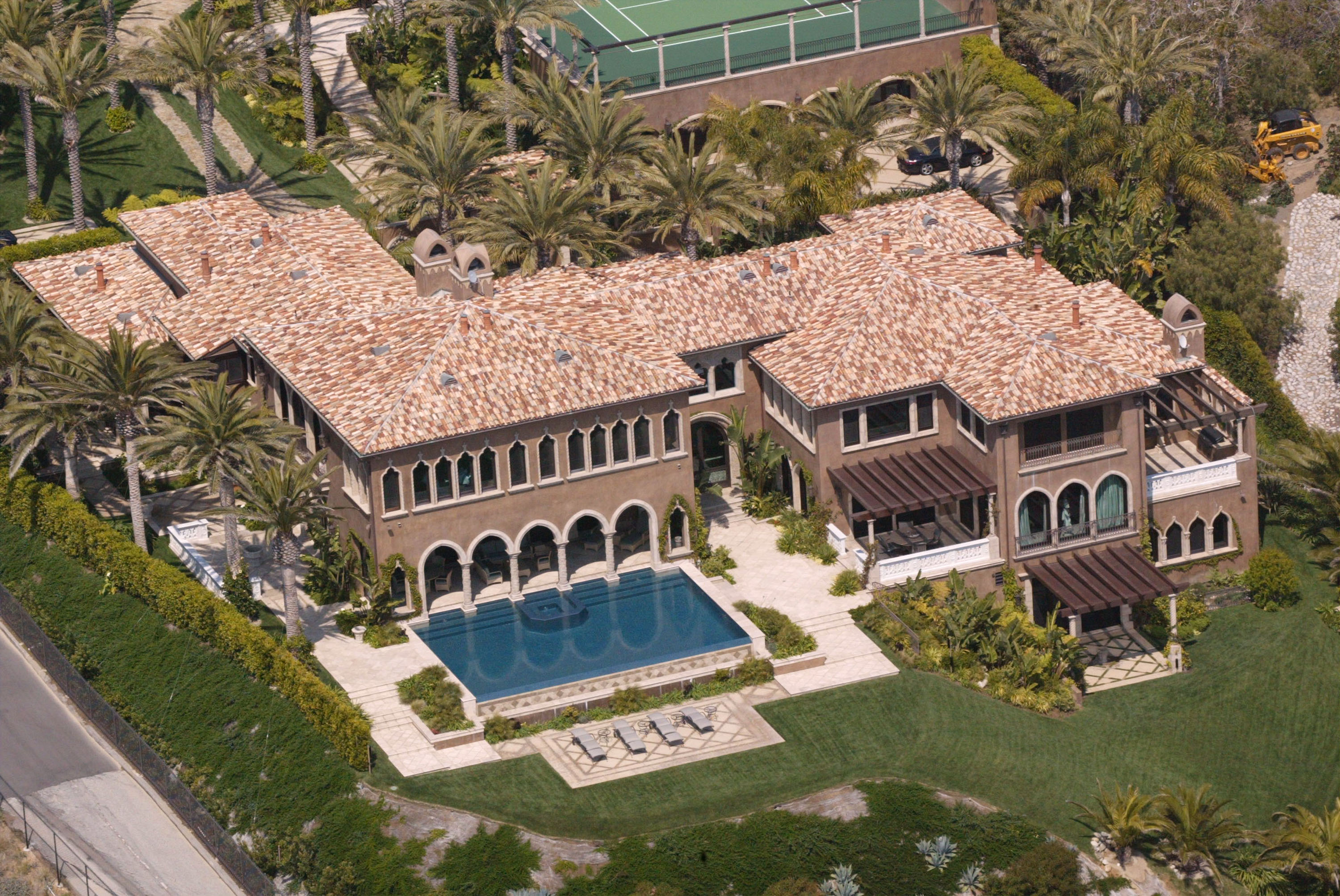 An aerial view captured Cher's luxurious Malibu estate on March 27, 2002, in Malibu, California. The sprawling Italianate mansion features clay-tile roofs, multiple arched loggias, a geometric infinity pool flanked by lounge chairs, and lush palm-lined grounds overlooking a private tennis court. | Source: Getty Images