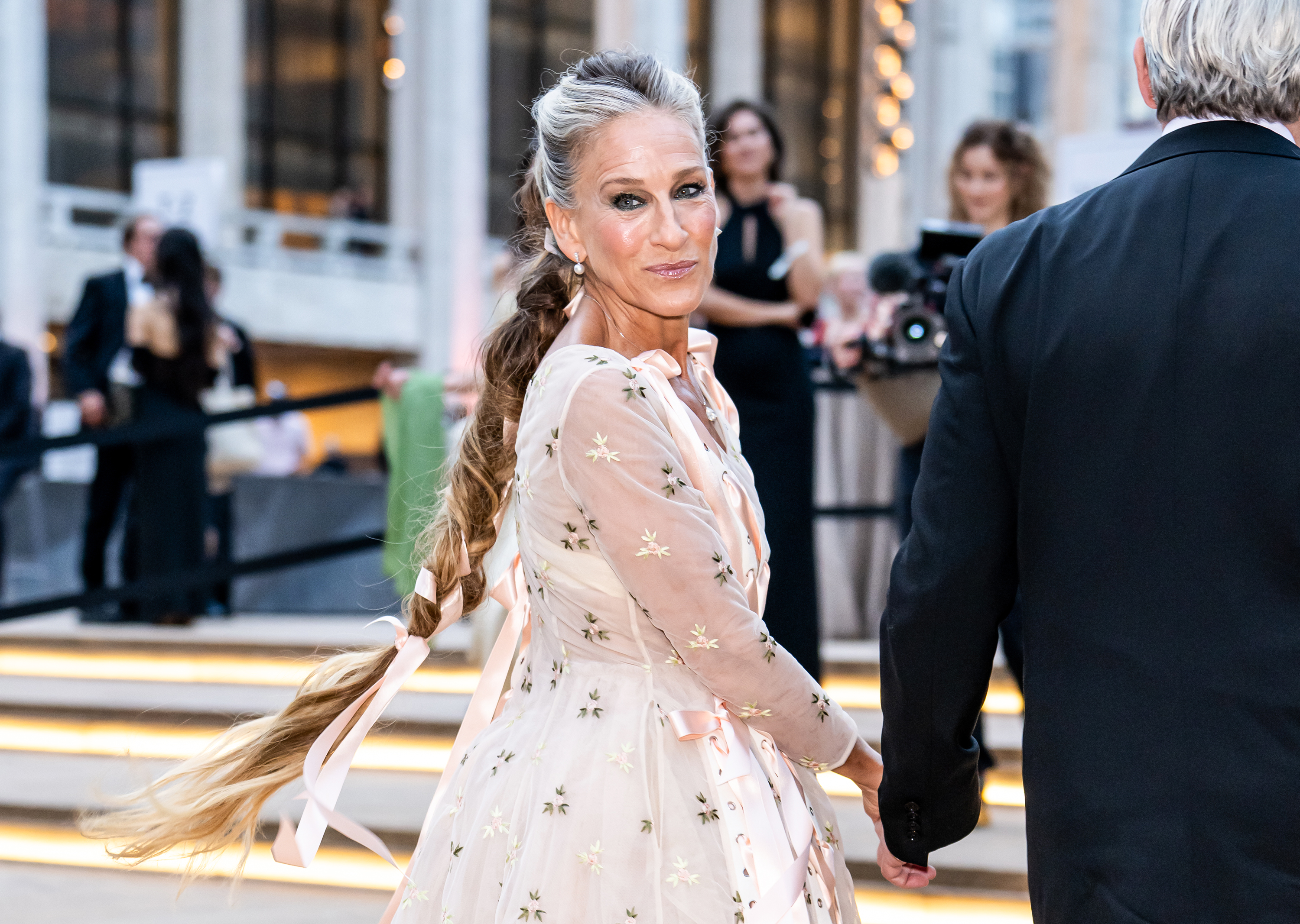 A side view captures Parker's ribbon-adorned ponytail cascading down her back as she arrives at the 2026 gala. Her hairstyle blends silver at the crown with darker lengths.