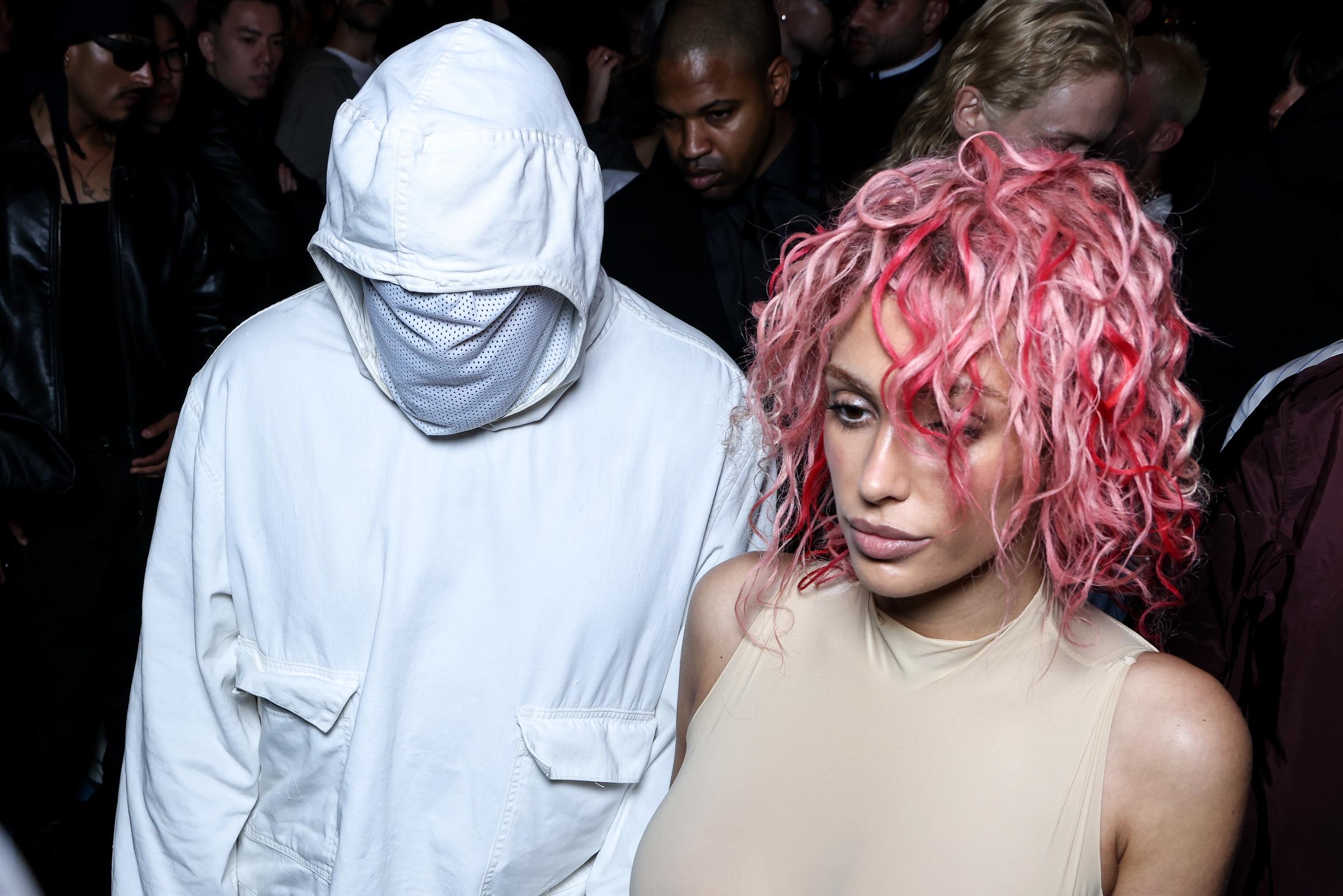 Bianca Censori stands in the foreground with pink hair as Kanye West appears behind her at Paris Fashion Week on June 19, 2024 | Source: Getty Images