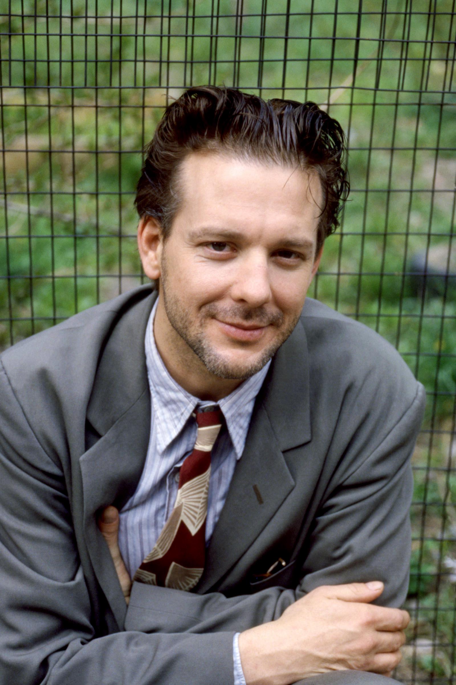A young Mickey Rourke poses with a subtle smile in New York, exuding effortless charm in a classic suit and patterned tie. With his slicked-back hair and relaxed posture, he captures the raw magnetism of rising stardom in that era.