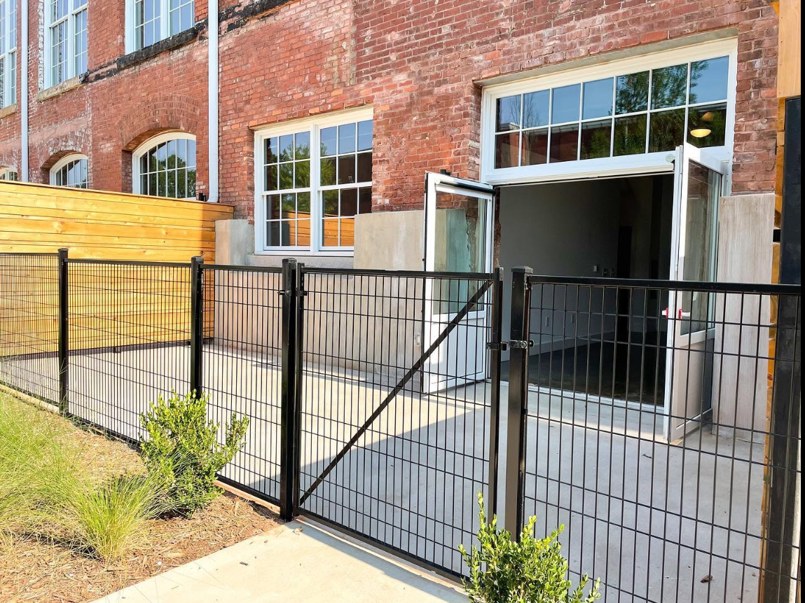 An exterior view shows one of the property's loft-style entrances, with the original brick facade, tall windows and a private fenced patio adding to the complex's distinctive character.