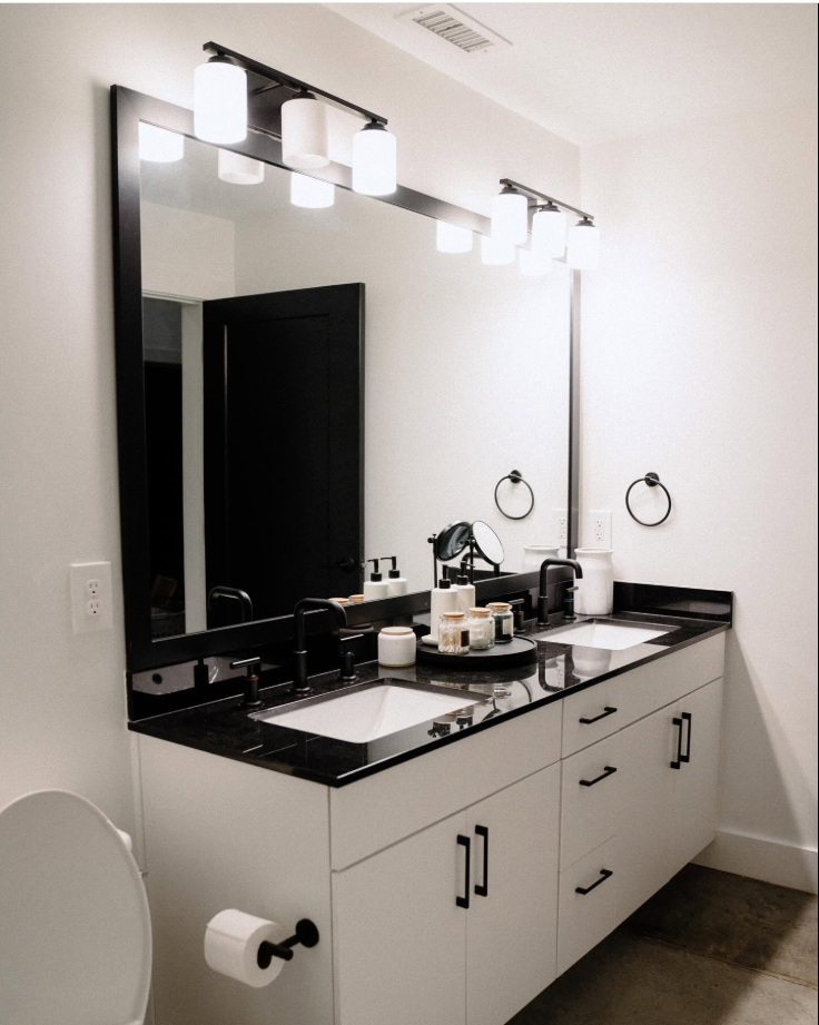 The bathroom carries the same clean, modern aesthetic, with a double vanity, black fixtures and hardware, and a wide mirror that brightens the space. | Source: Facebook/Judson Mills Loft
