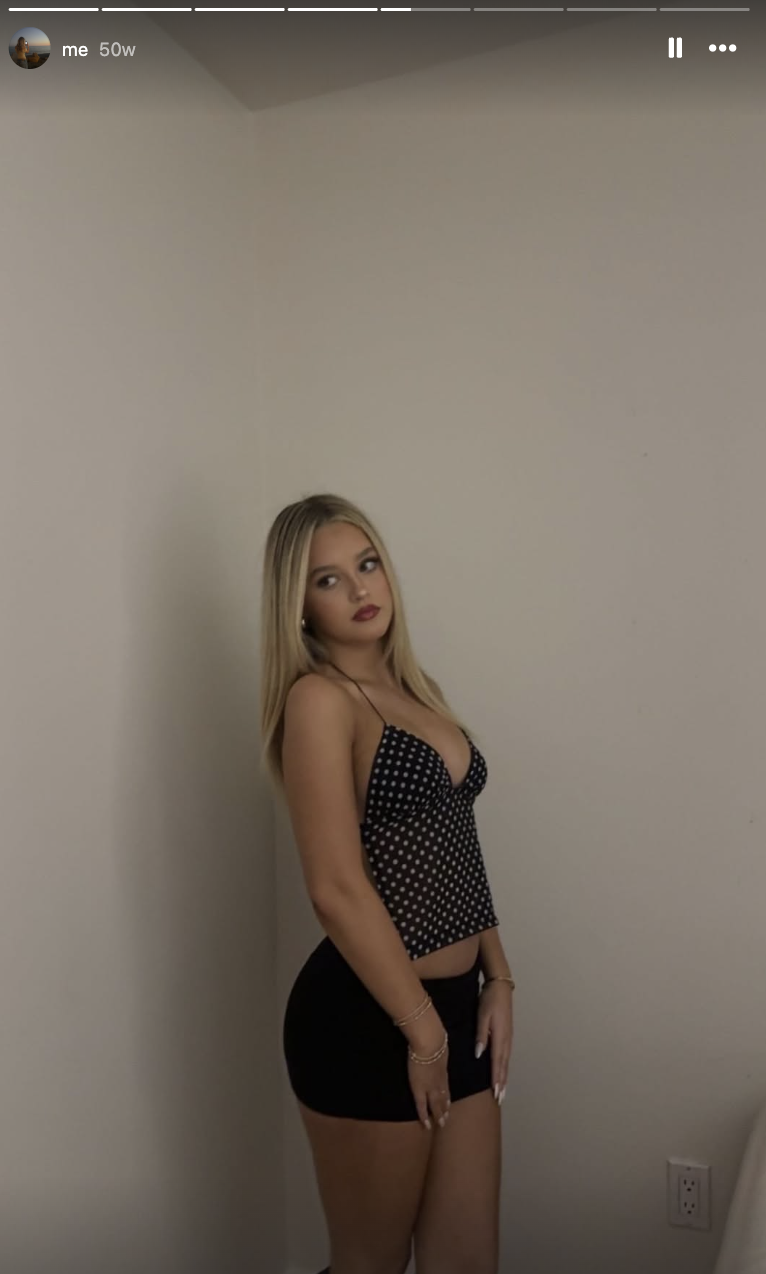 Finley Lockwood poses in front of a neutral backdrop, wearing a black-and-white polka-dot halter neck top paired with a fitted black mini skirt, styling her long blonde hair straight with a center part.