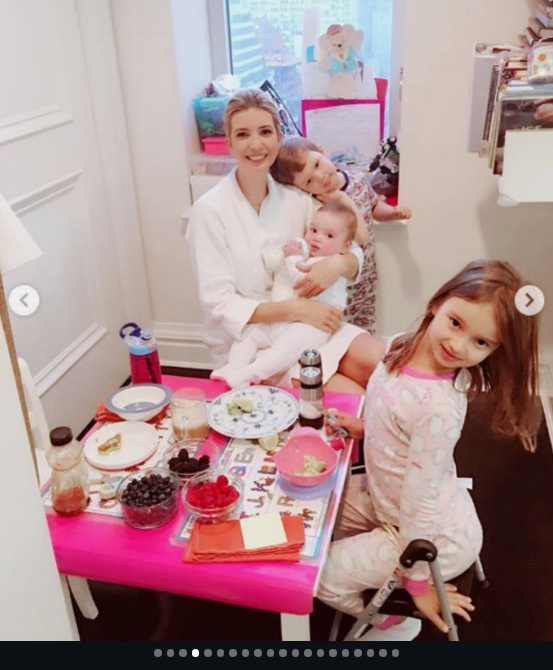 A nostalgic domestic throwback showed Arabella sitting at a pink-topped children's activity table in printed pajamas, looking up at the camera during breakfast. Behind her, Ivanka Trump relaxed in a white robe, cradling a baby while daughter and younger brothers gathered for morning fruit and snacks. | Source: Instagram/ivankatrump