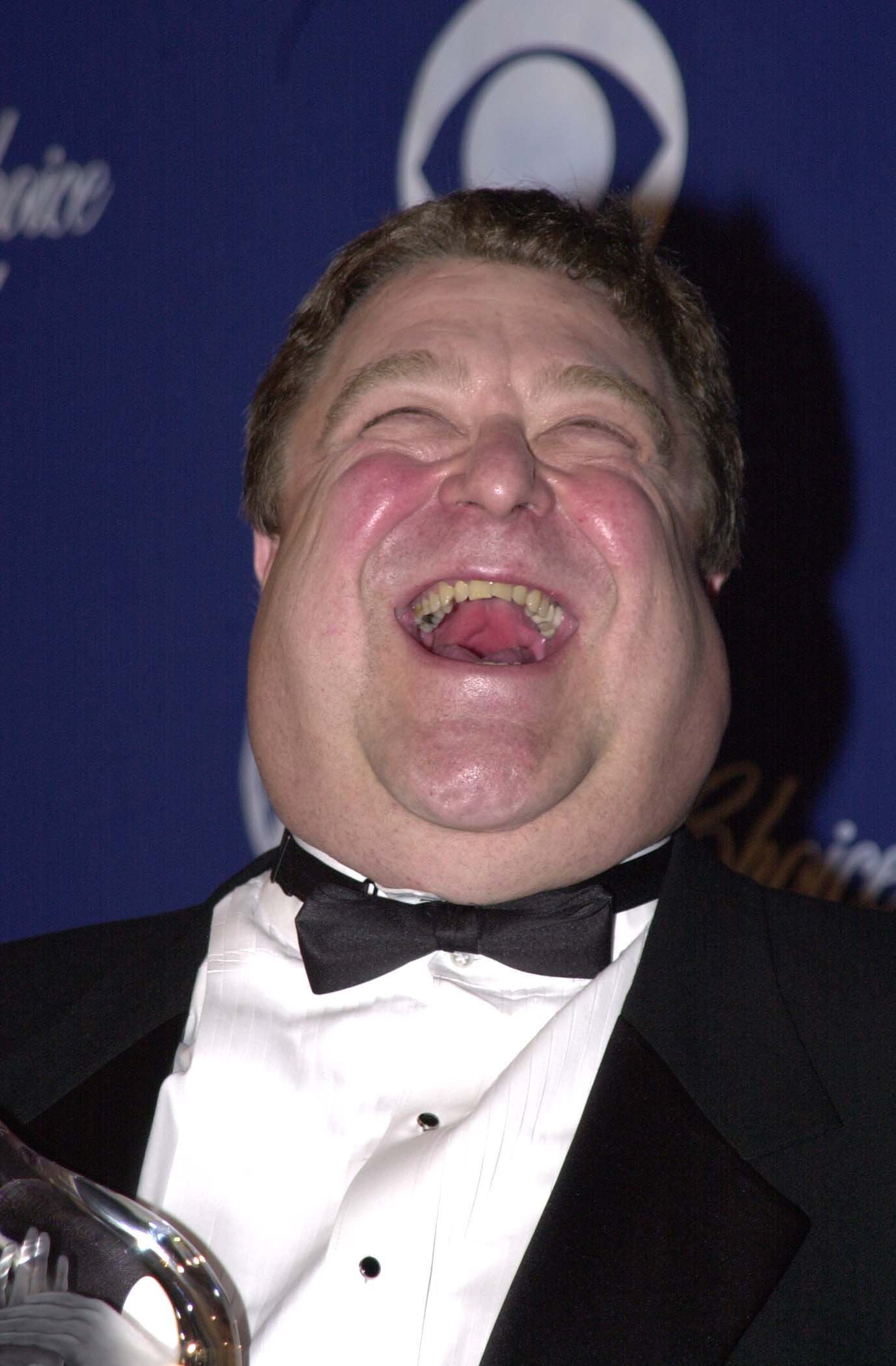 Goodman laughed during the 2001 People's Choice Awards in a black tuxedo. The photo shows his fuller build before his later weight loss. | Source: Getty Images