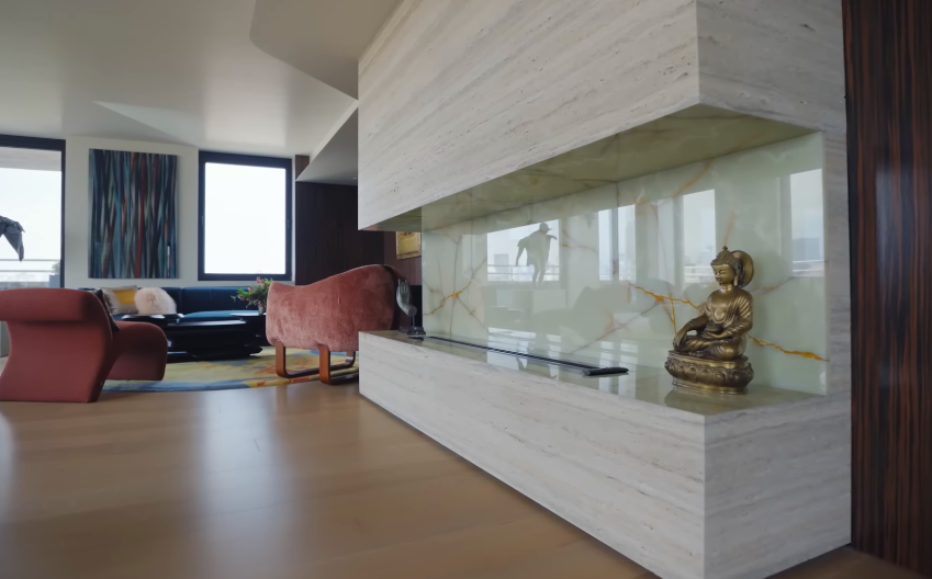 The fireplace doubles as a display ledge, with a Buddha sculpture adding another personal object to the highly finished architecture. Even here, the family resisted making the room feel too formal or untouched. | Source: YouTube/Architectural Digest