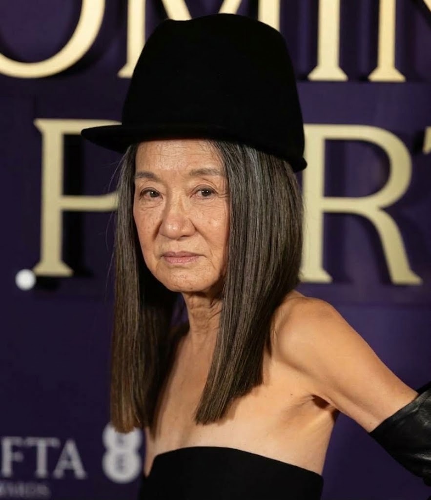 Inspired by her appearance on the 2026 BAFTA red carpet, this AI concept imagines Vera Wang with authentic mature facial contours, delicate under-eye lines, and silver-dusted dark hair falling in a blunt cut. Topped with a tall black cloche hat and styled in a strapless black neckline with matching leather opera gloves against a purple step-and-repeat board, the rendering offers a realistic look at the icon aging conventionally. | Source: Gemini