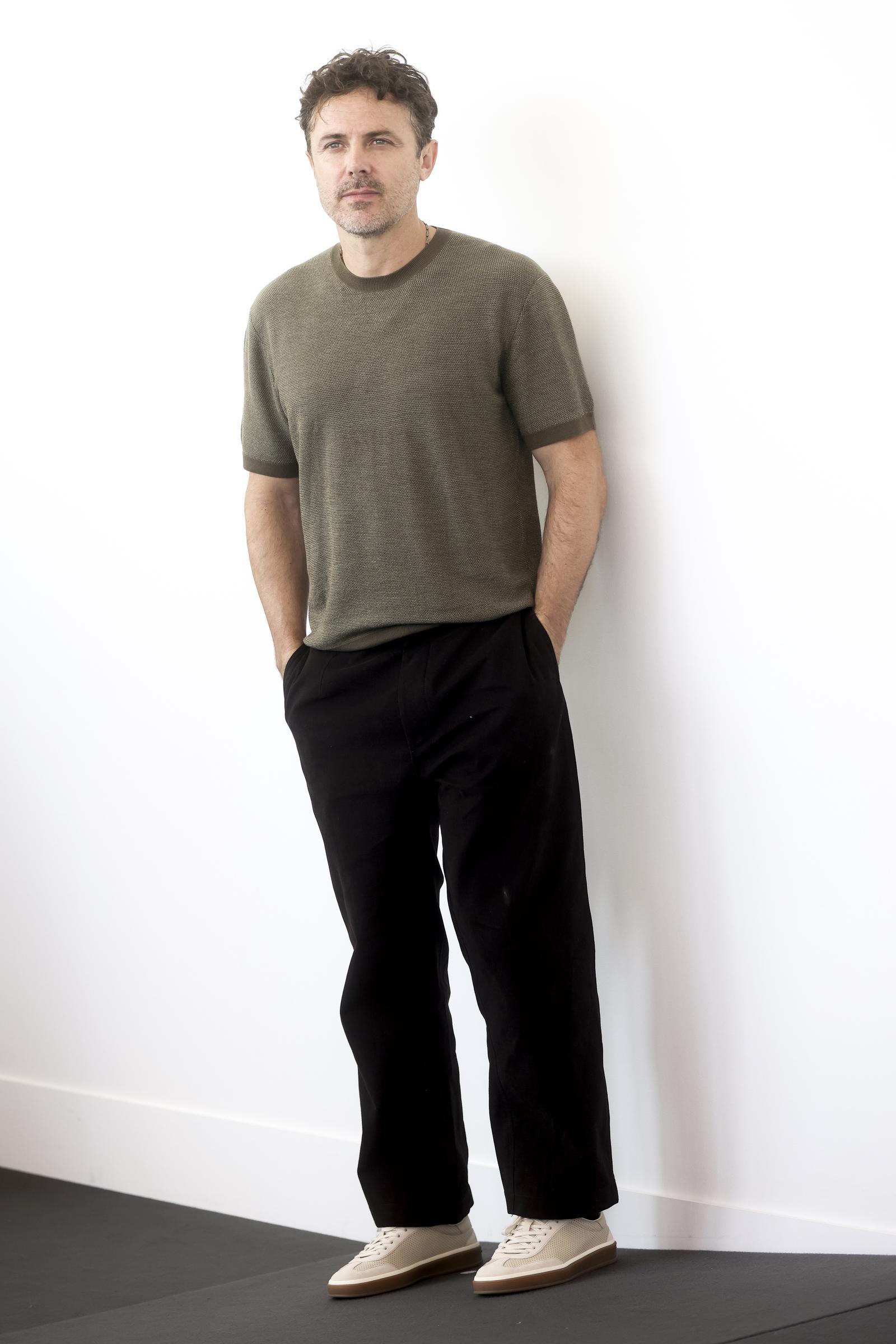 Leaning into an earthy, minimalist palette, Casey Affleck paired a fine-knit, short-sleeved olive crewneck with slouchy, wide-leg black trousers at the "Company" photocall at Palazzo del Casino on September 8, 2026. Two-tone cream sneakers with caramel gum soles lent a relaxed skate-inspired finish to his daytime festival appearance. | Source: Getty Images