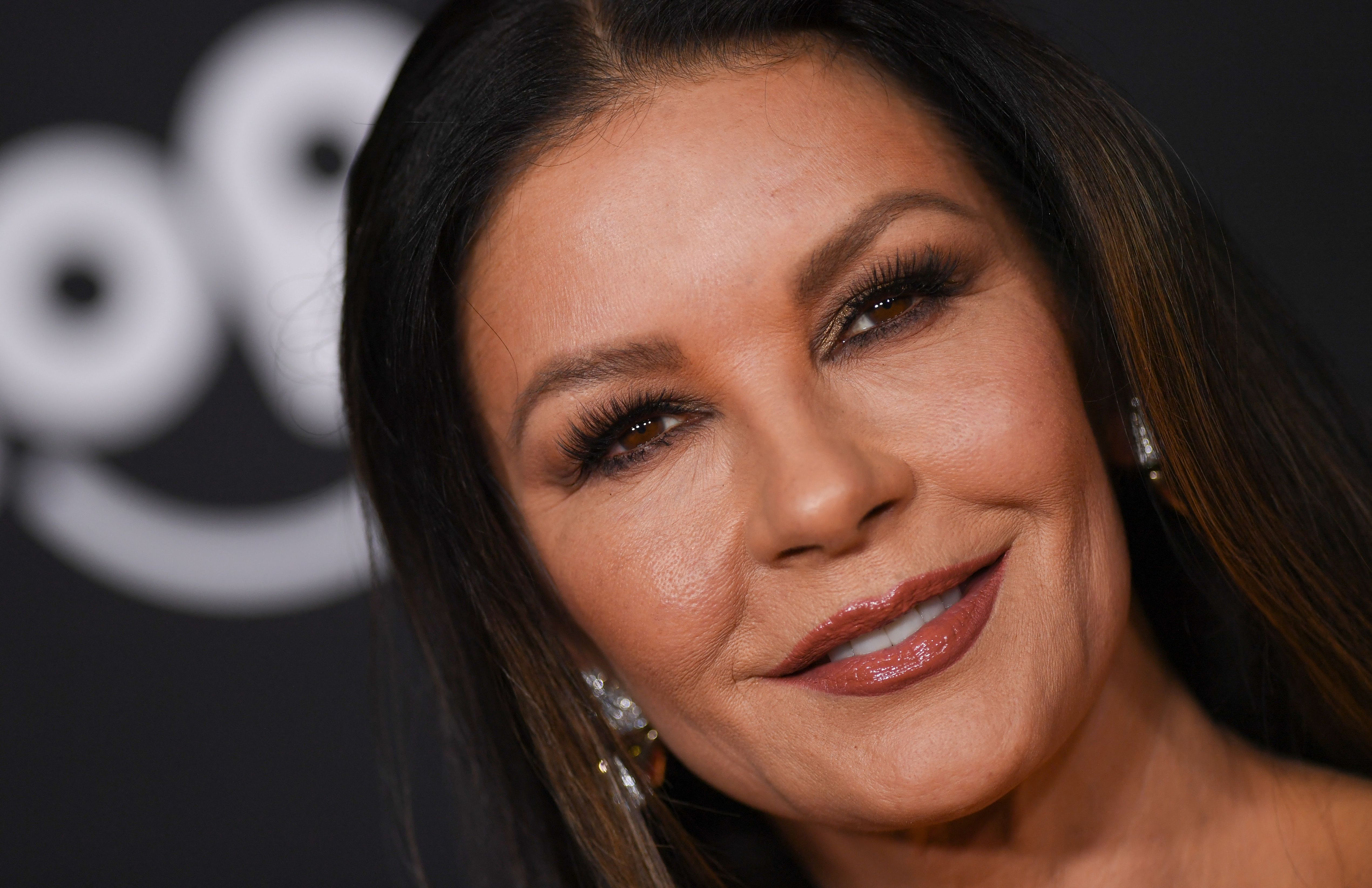 Catherine Zeta-Jones poses for a close-up portrait on the red carpet at the world premiere of Marvel Studios' "Ant-Man and the Wasp: Quantumania" at the Regency Village Theatre on February 6, 2023, in Los Angeles, California. The Welsh actress smiles warmly, highlighting a golden-bronze smoky eye, full lashes, a glossy mauve lip, and sparkling diamond earrings nestled against her sleek brunette hair.