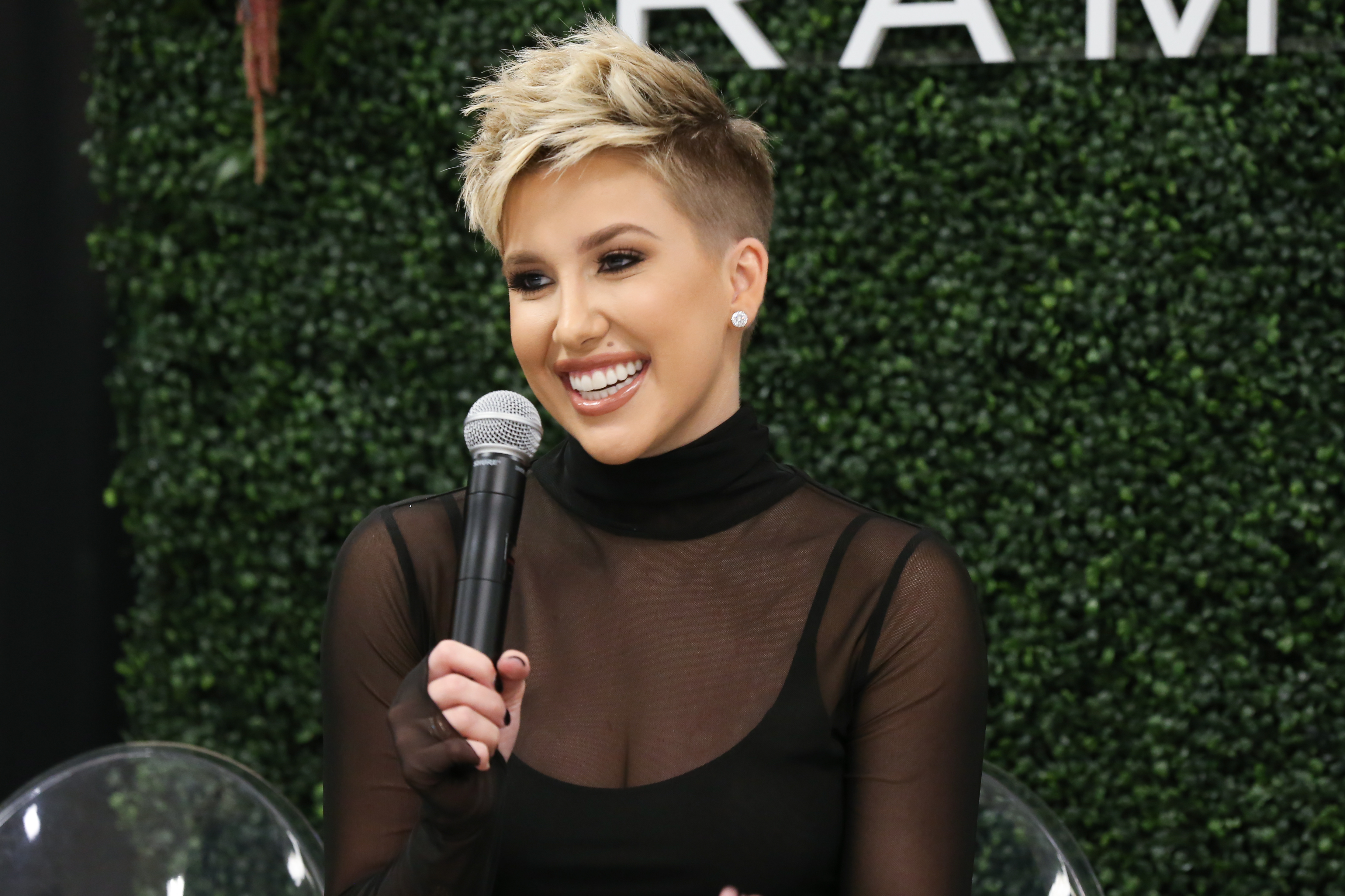 Savannah Chrisley smiles while speaking into a microphone during a personal appearance for Rampage at Belk in Cool Springs Galleria Mall in Franklin, Tennessee, on November 5, 2019, wearing a sheer black turtleneck top over a dark tank and styling her blonde hair in an edgy, textured pixie cut. | Source: Getty Images
