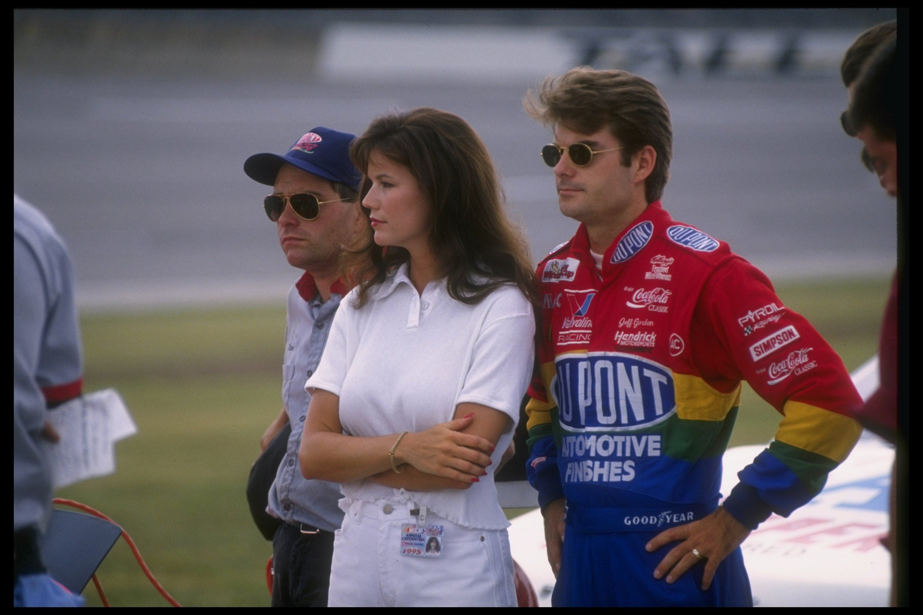 Jeff Gordon stood beside his then-wife, Brooke Sealey, as they watched the qualifying heats for the NASCAR DieHard 500 at Talladega Superspeedway on July 21, 1995. With Gordon in his colorful racing suit and Sealey at his side, the couple shared a quieter trackside moment during the early years of their marriage.