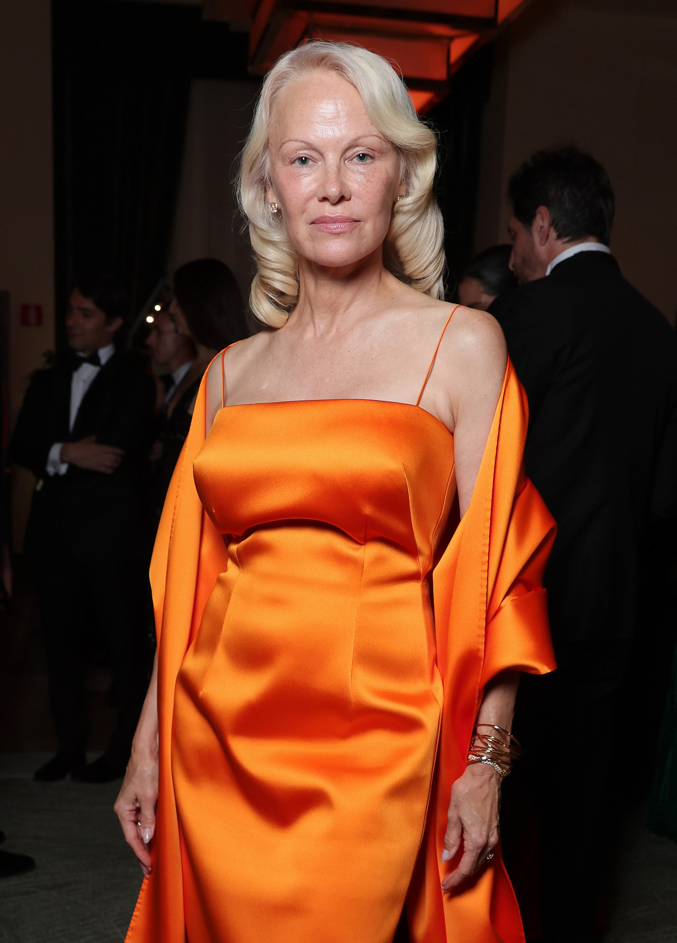 Pamela Anderson paired her signature platinum blonde curls with a striking orange satin gown, proving that her Hollywood style has evolved far beyond the glamorous Baywatch image of the 1990s. | Source: Getty Images