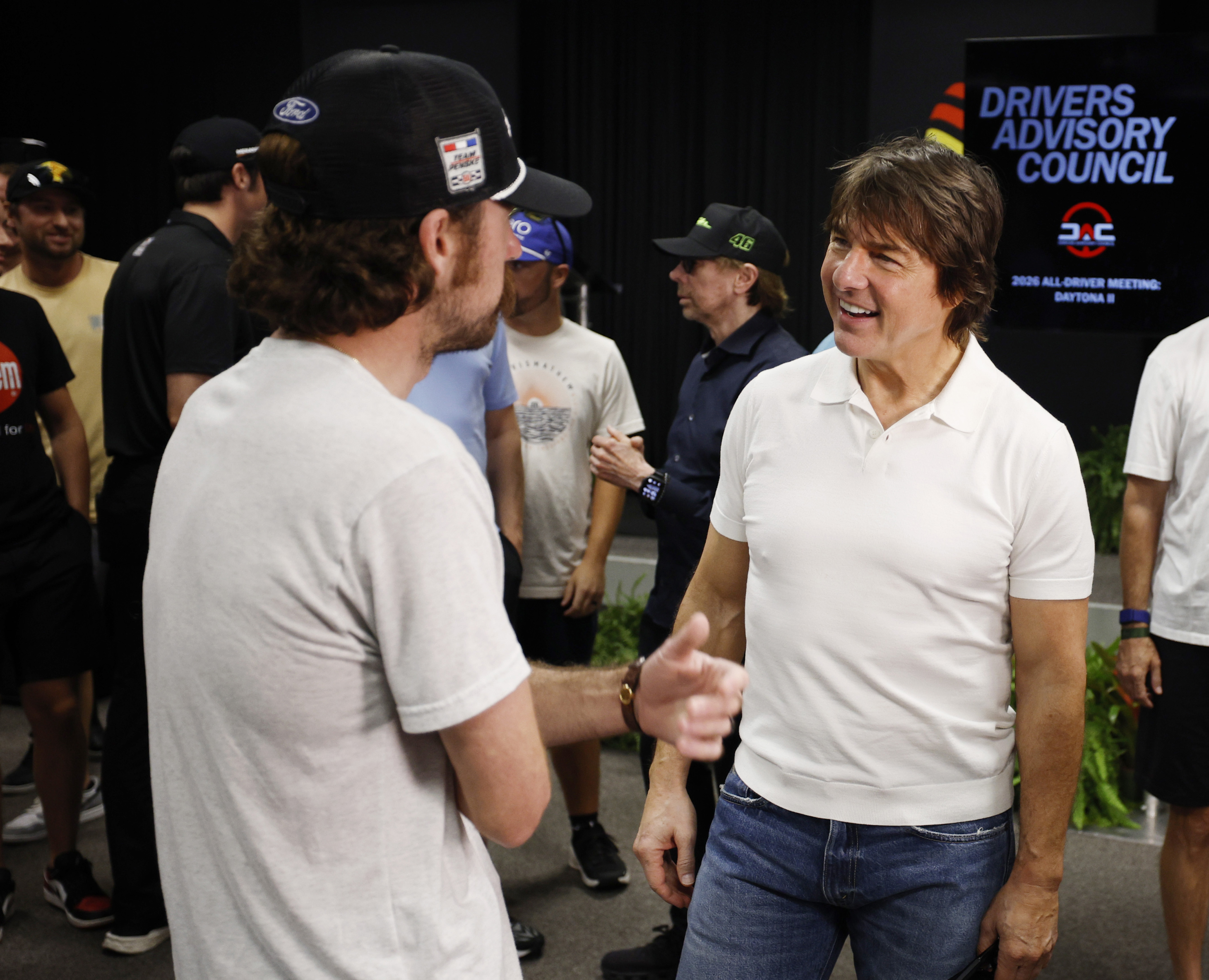 Inside the drivers' meeting, Cruise smiles while speaking with an attendee. Without his sunglasses, his face and brown hair are more clearly visible in the close-range photo. | Source: Getty Images