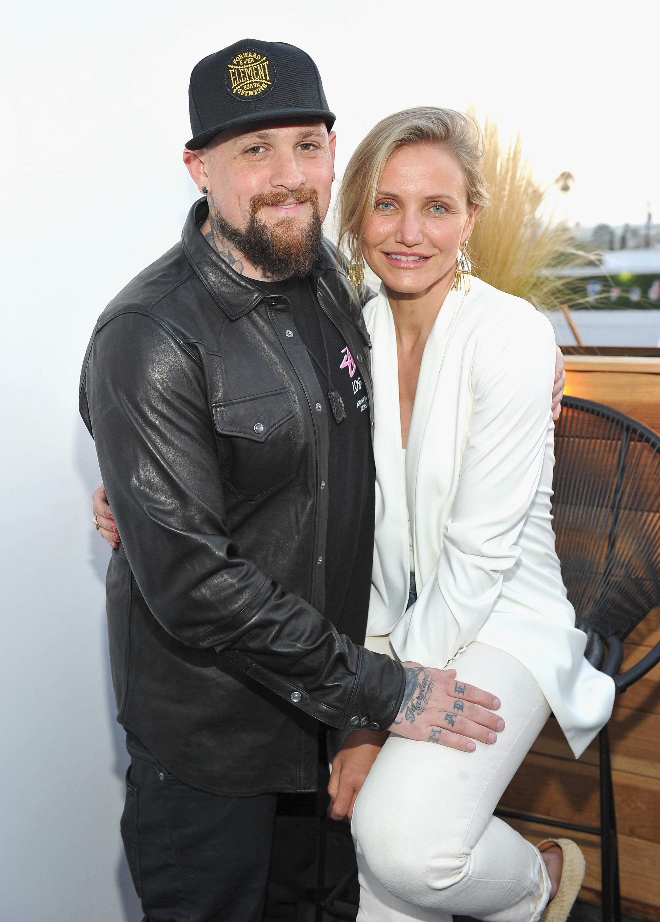 Still at the House of Harlow celebration, Cameron Diaz perched on a stool while her husband Benji Madden leaned in close, his hand resting protectively on her leg. Smiling at the camera in coordinated monochrome looks — Cameron in crisp white, Benji in sleek black leather — the couple radiated unity and ease as they posed together.