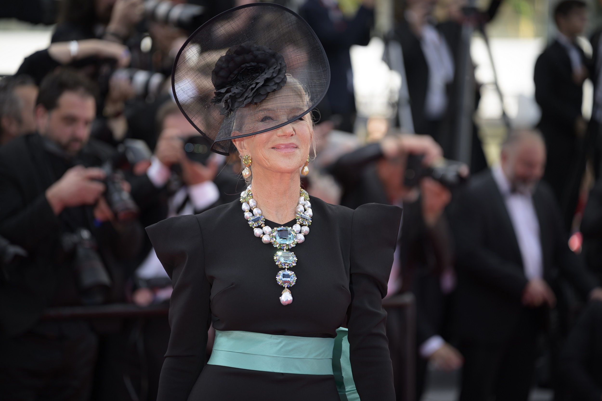 Mirren’s serene smile radiates composure, while her necklace commands attention like a regal crest. With its cascade of luminous stones and pearls, the piece mirrors her presence — both unmistakably the centerpiece in a sea of flashbulbs.