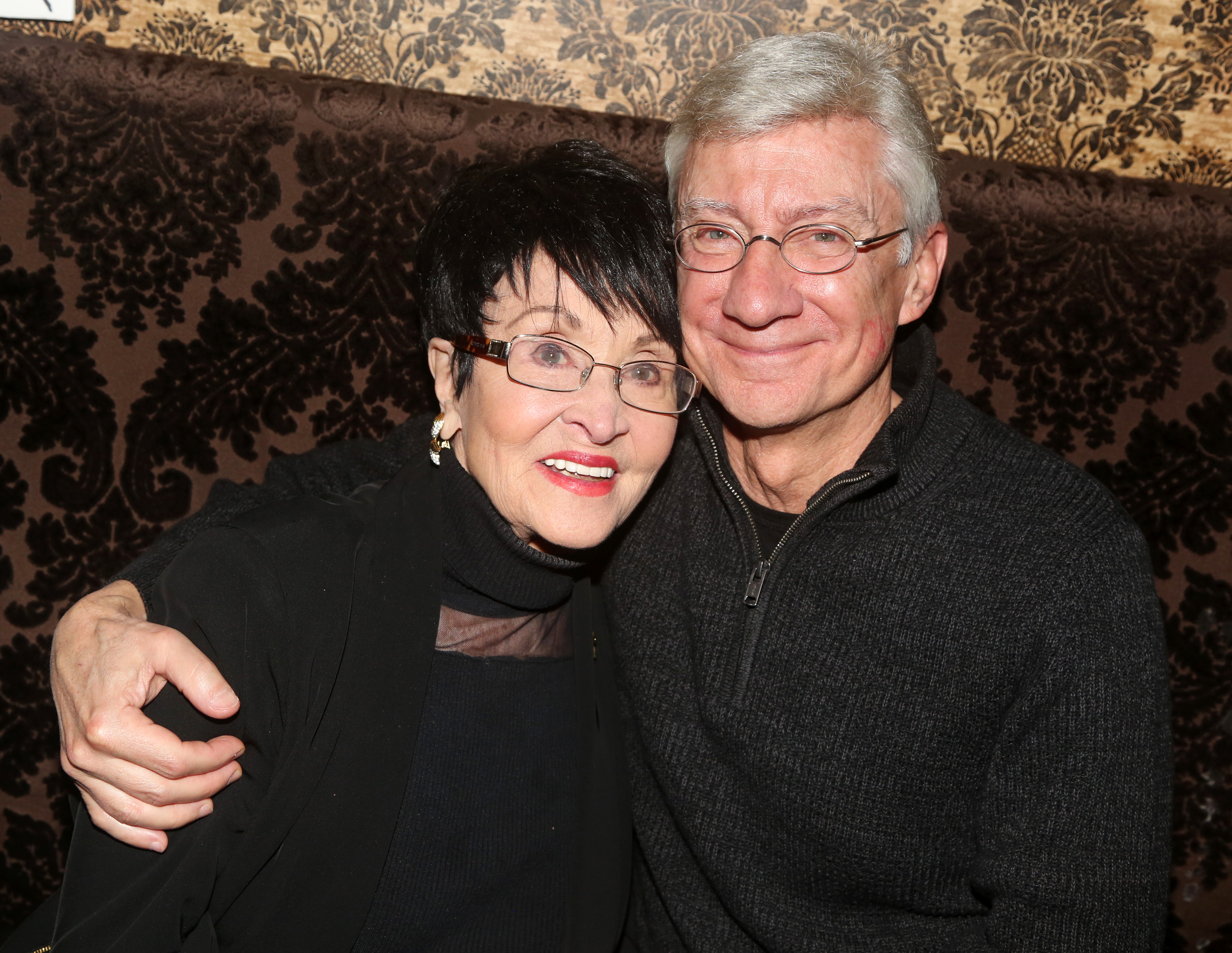 Chita Rivera and David Garrison posed closely together during Rivera's 90th birthday celebration at Bathtub Gin on January 23, 2023, in New York City. The longtime stage and television veterans shared a warm embrace, with Garrison in oval glasses and a charcoal quarter-zip sweater wrapping his arm around Rivera, who looked radiant in a chic black turtleneck top, rectangular frames, and a vibrant red lip. | Source: Getty Images