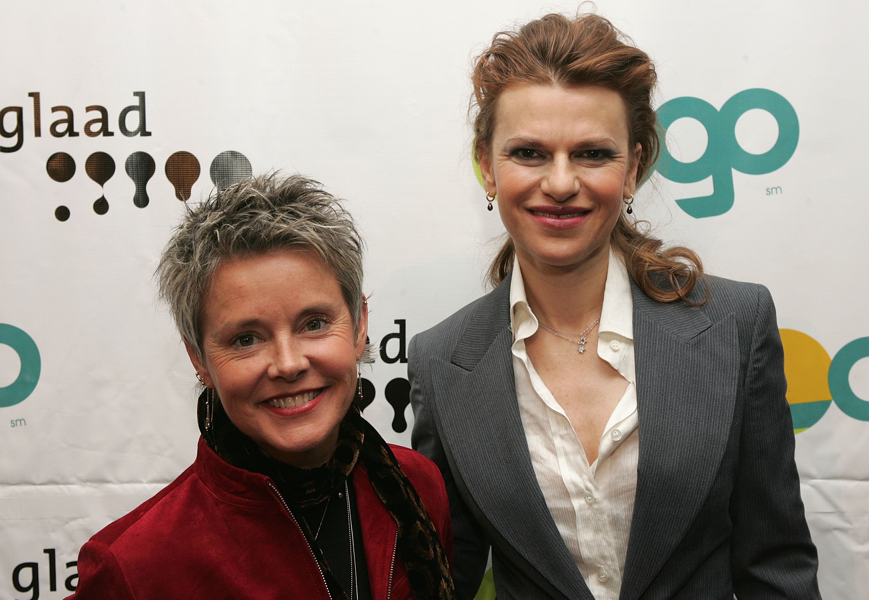 Amanda Bearse and Sandra Bernhard smiled side by side while attending the 17th Annual GLAAD Media Awards at the Marriott Marquis Hotel on March 27, 2006, in New York City. The actresses posed together in front of the step-and-repeat backdrop, with Bearse sporting her signature cropped pixie cut in a rich red velvet jacket with a leopard-print scarf accent, while Bernhard opted for a tailored grey pinstripe pantsuit over an open-collar white blouse. | Source: Getty Images