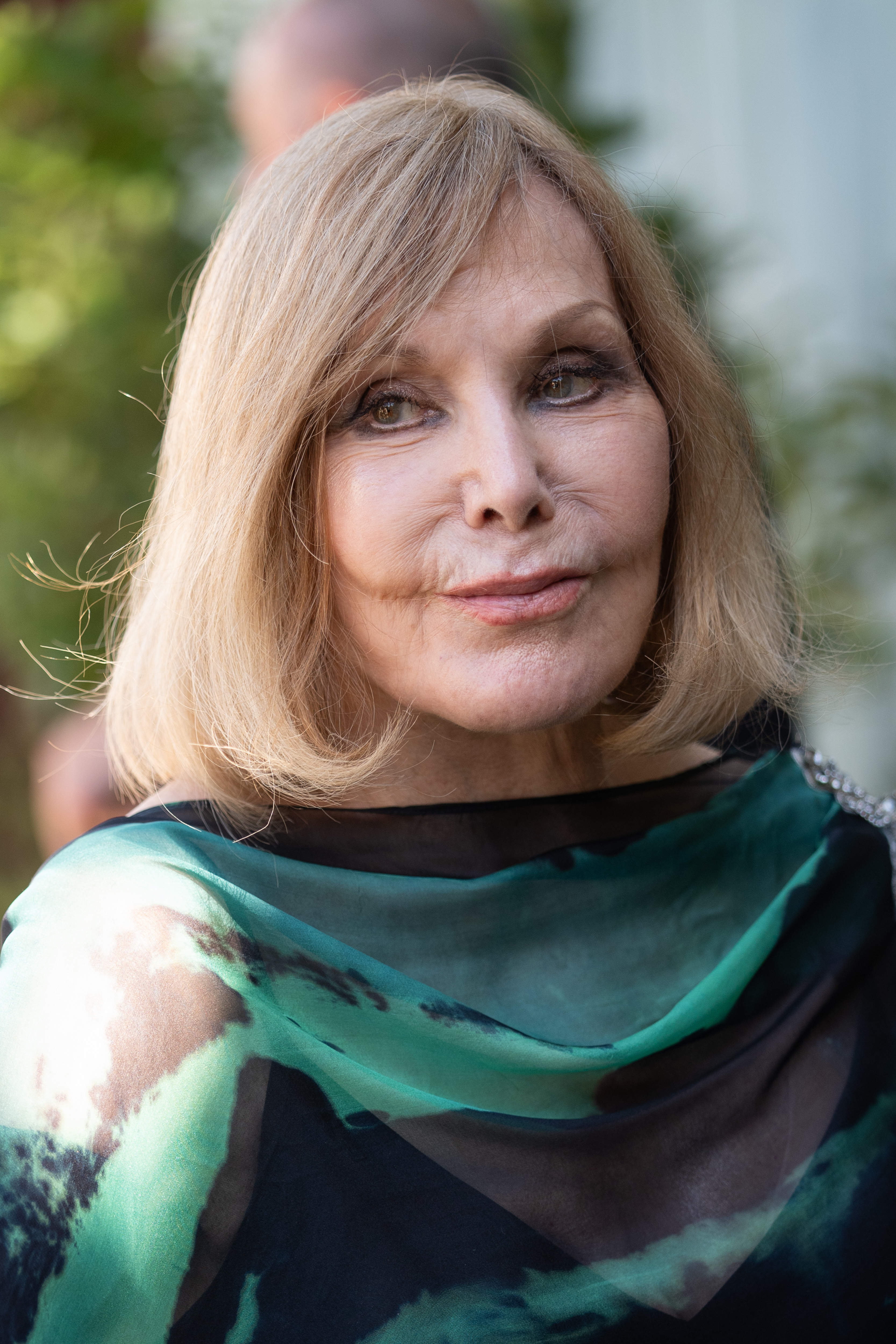 Kim Novak poses for a close-up portrait at the 82nd Venice International Film Festival, wearing a teal-and-green patterned wrap over a black outfit. Her blonde bob frames her face as she looks slightly to the side. | Source: Getty Images