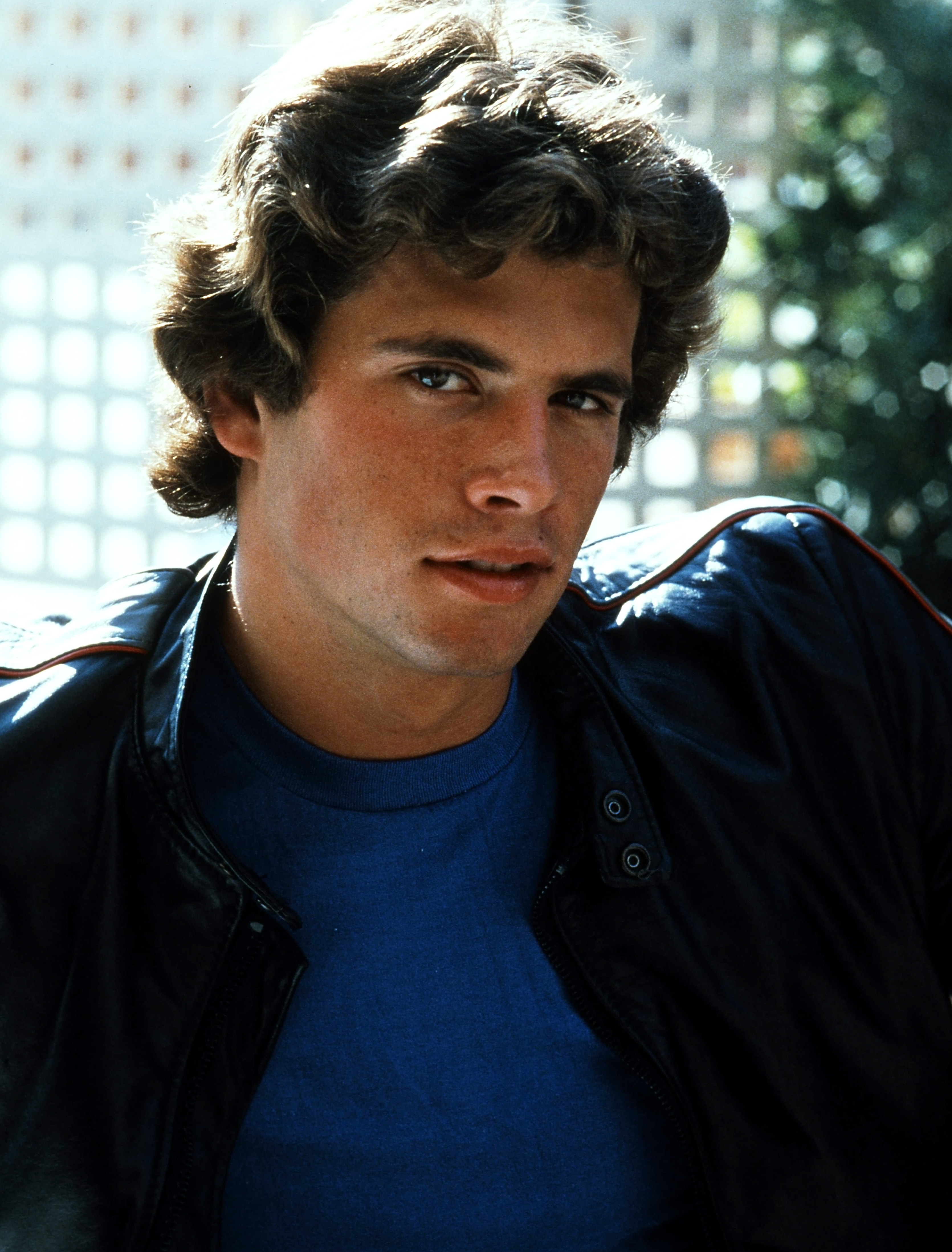 The rising actor channels effortless cool in a vintage color portrait from circa 1978. Sporting a vibrant blue crewneck t-shirt beneath a black leather jacket with red trim, he looks into the camera with voluminous, sun-kissed brunette curls and sharp, chiselled features. | Source: Getty Images