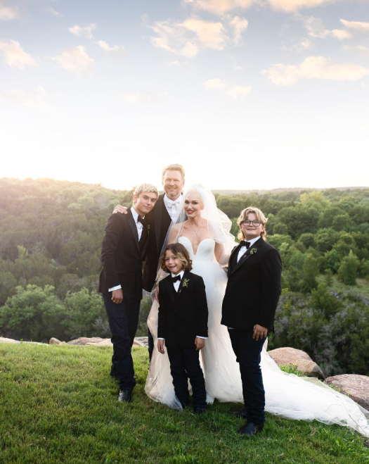 Gwen Stefani and Blake Shelton celebrated their wedding day surrounded by her three sons, Kingston, Zuma, and Apollo Rossdale, all dressed in classic black tuxedos. In this photo, they posed together against a scenic outdoor backdrop on an image shared on July 7, 2021. | Source: Instagram/gwenstefani