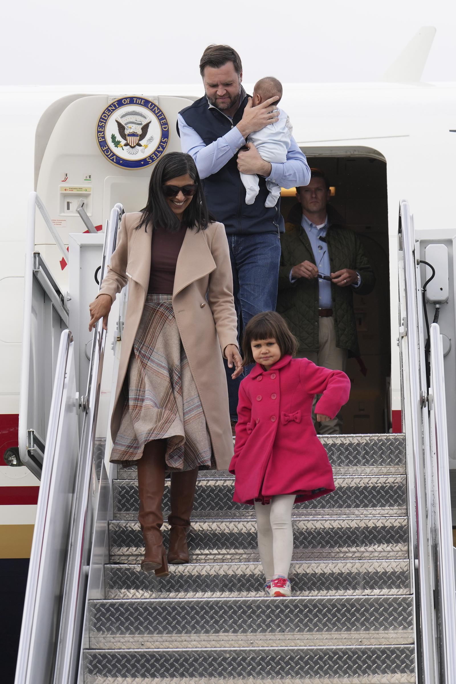 Usha Vance and daughter Mirabel walk ahead as JD carries Alec down the aircraft steps, with Mirabel's bright coat standing out in the family arrival. | Source: Getty Images