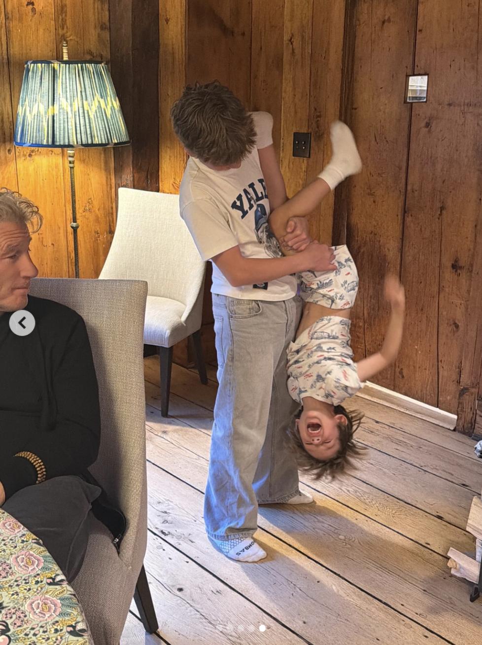 Richard Gere looks on as children play indoors in a cozy room featuring wood-paneled walls, rustic flooring, and soft lighting. | Source: Instagram/alejandragere